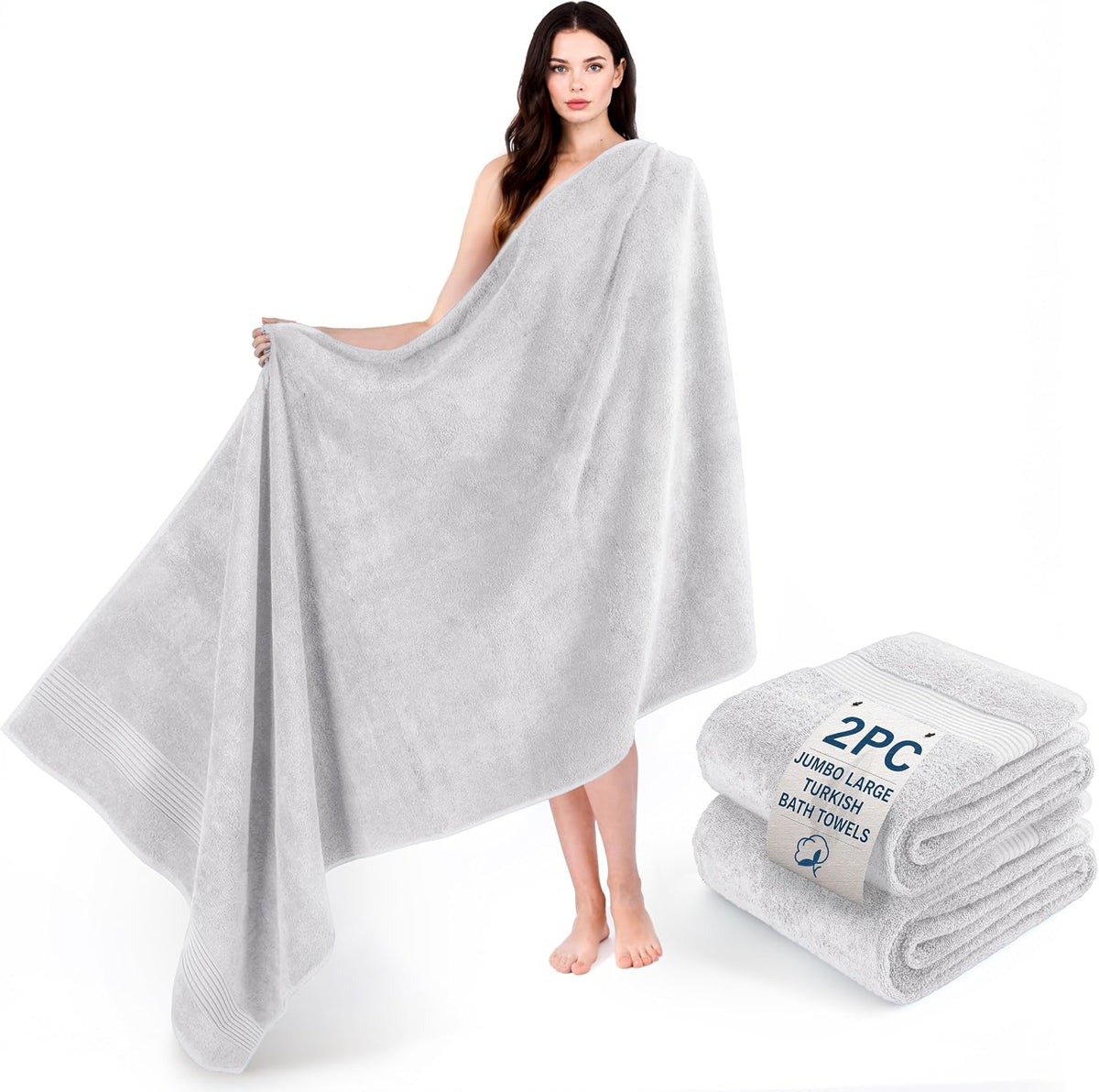 Model holding open a large snow-white bath towel beside a folded pair of white towels.