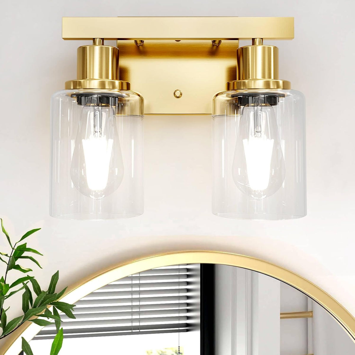 Two-light wall sconce with clear cylindrical glass shades and warm gold finish mounted above a mirror