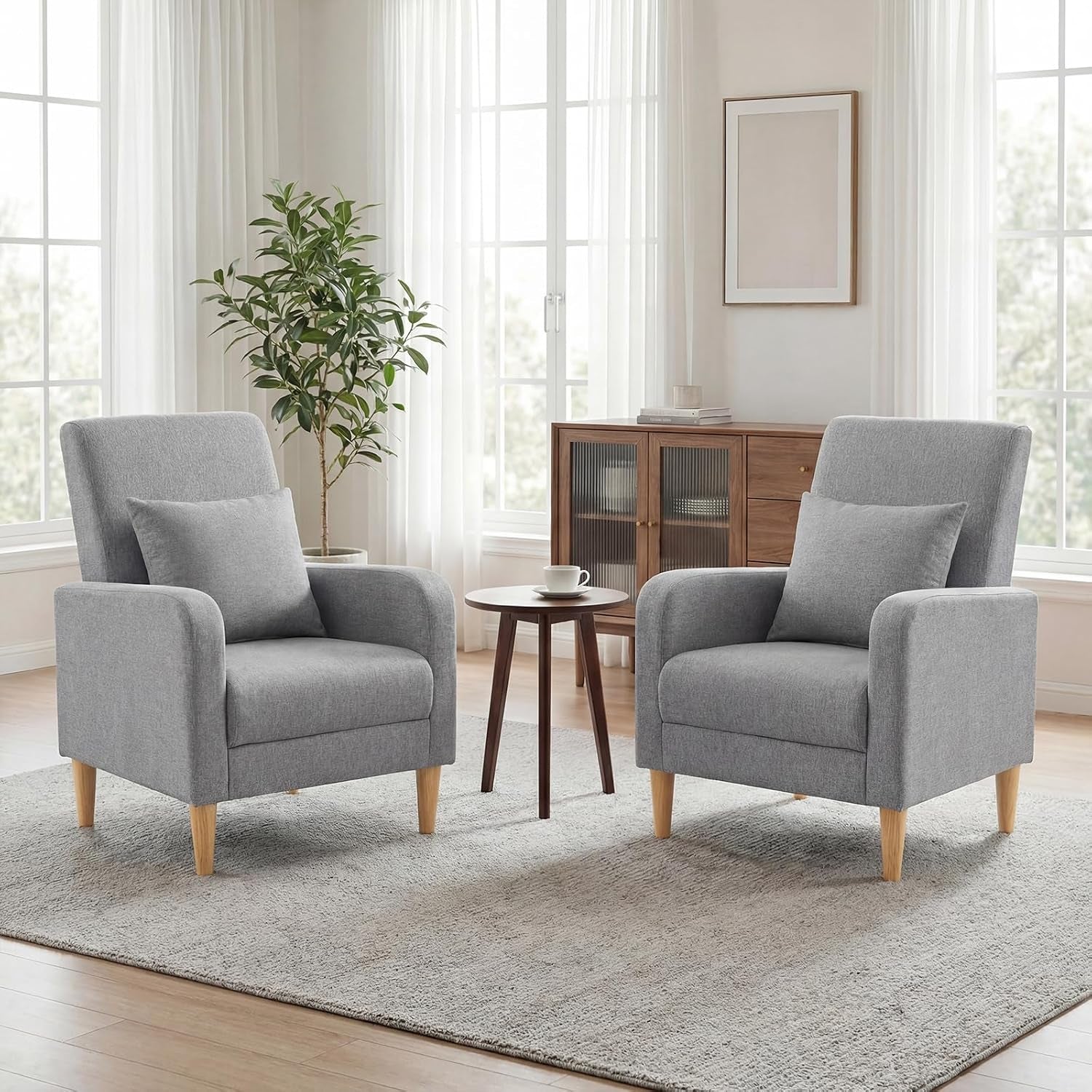 Two light gray fabric armchairs with wooden legs flanking a small round table on a textured rug.