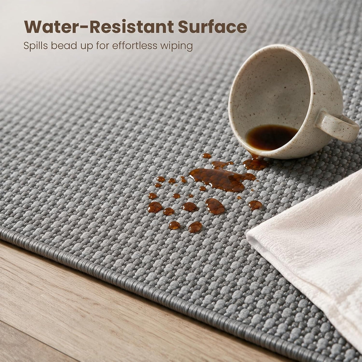 Detail of spilled liquid beading on grey rug surface near the bound edge demonstrating the water-repellent finish