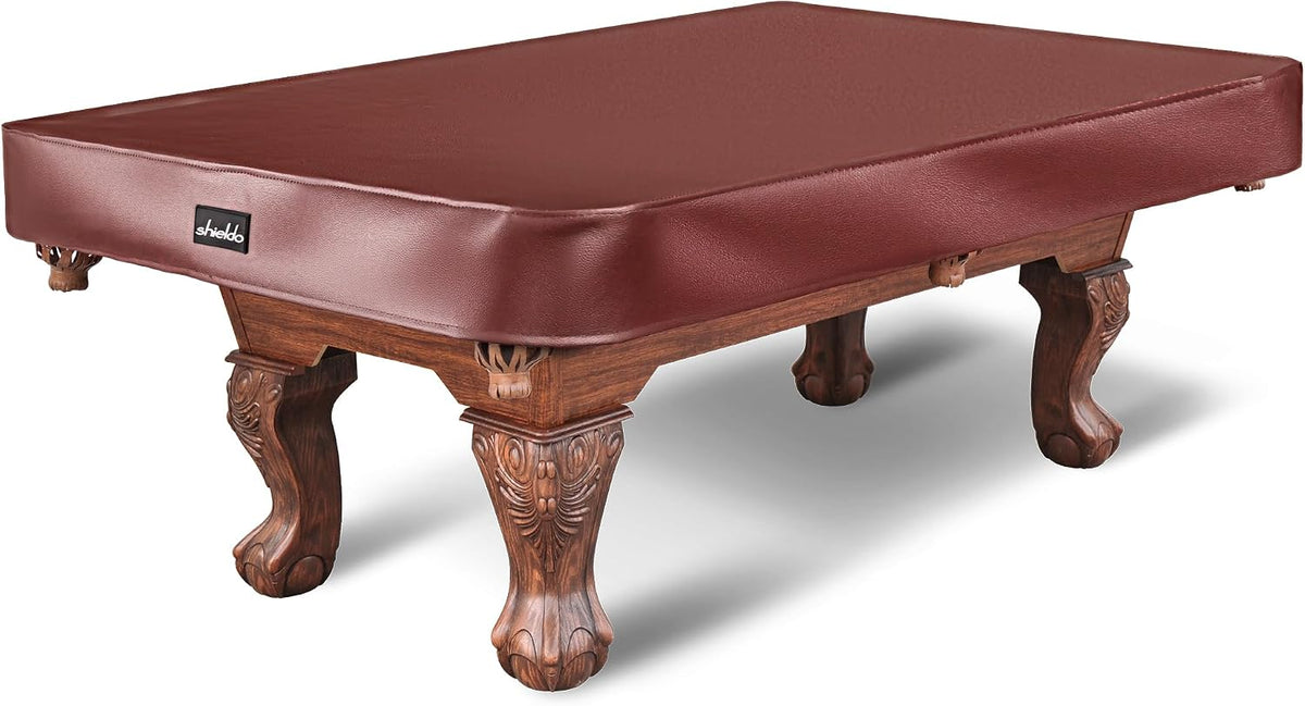 Angled view of a burgundy leatherette pool table cover fitted over a carved wooden pool table.