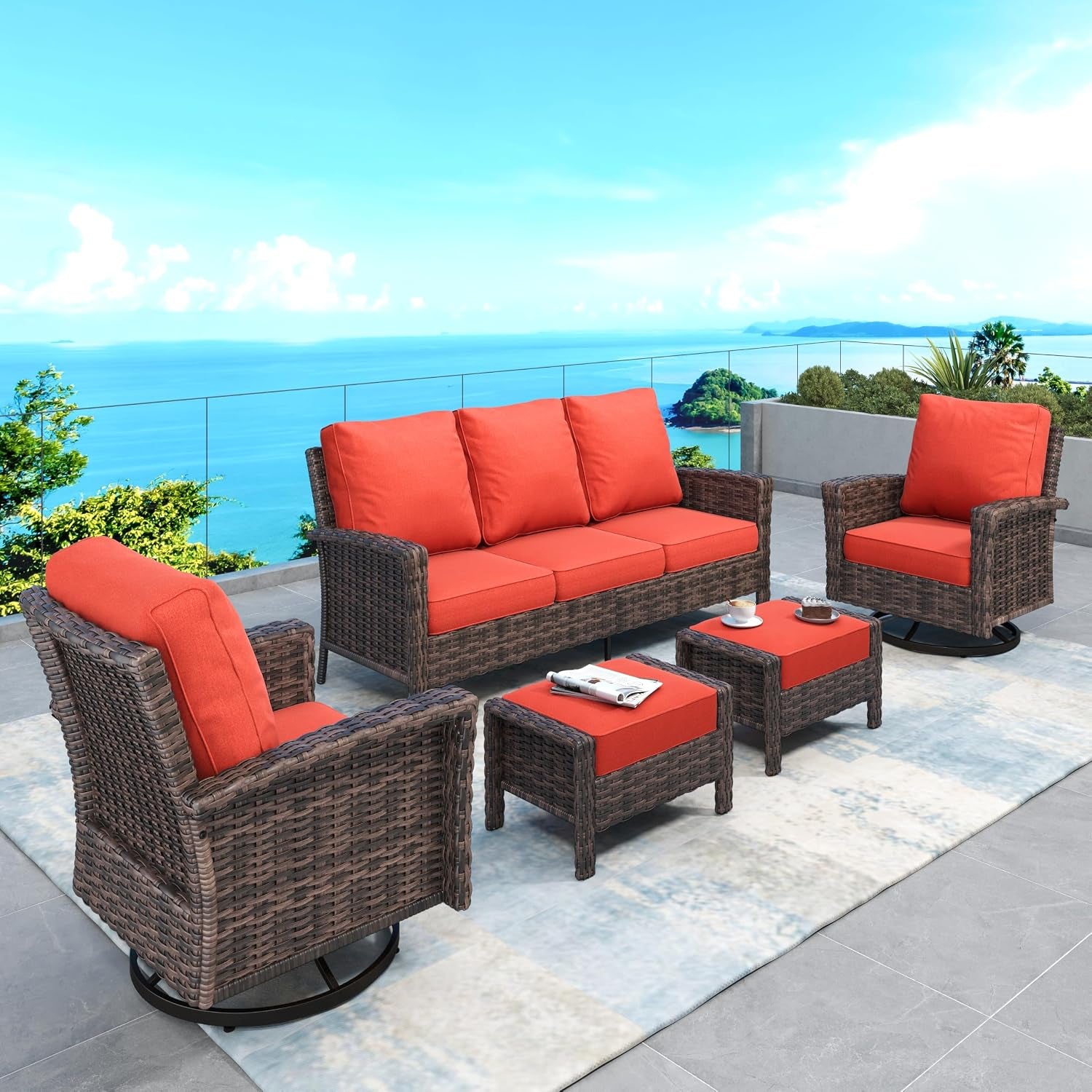 Outdoor brown wicker sofa set with bright red cushions arranged on a tiled terrace overlooking the ocean.