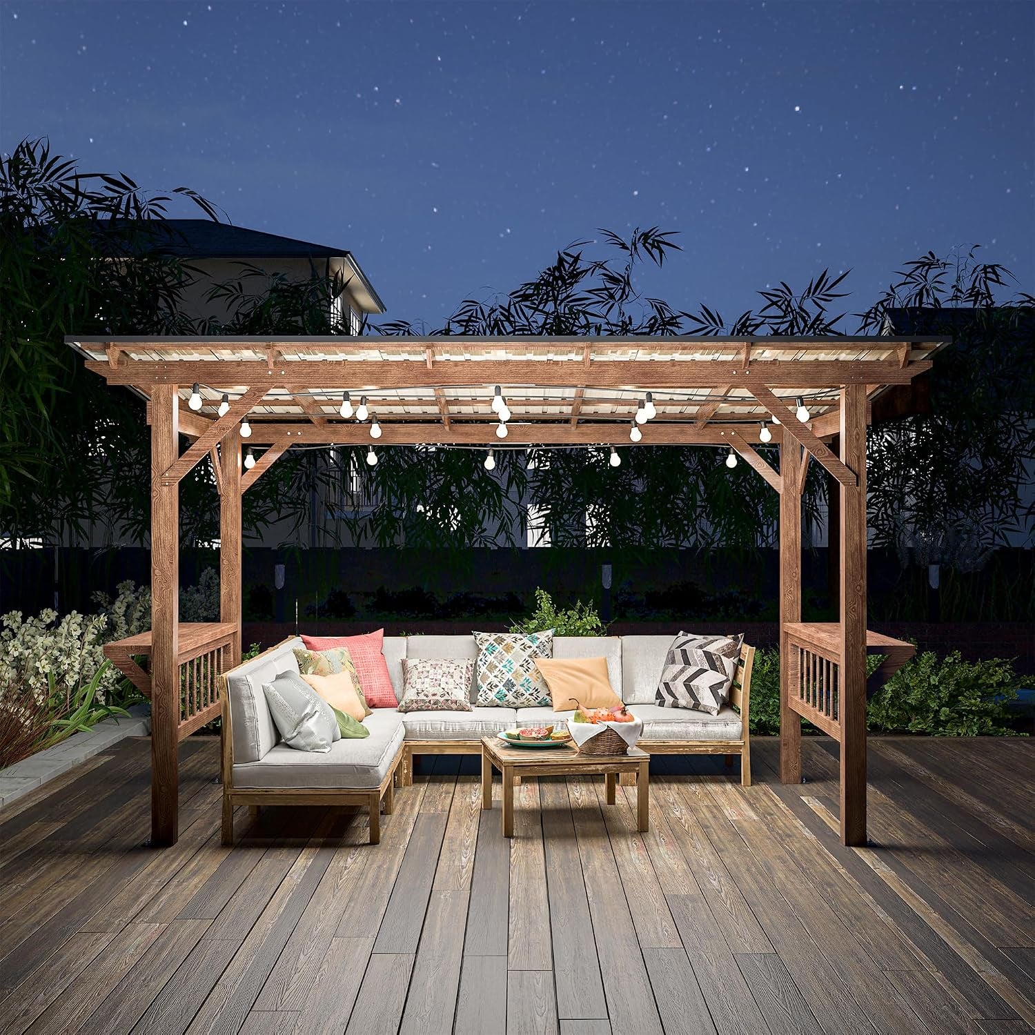 Wide outdoor view of a wooden gazebo on a deck with sectional seating, patterned pillows, coffee table, and string lights