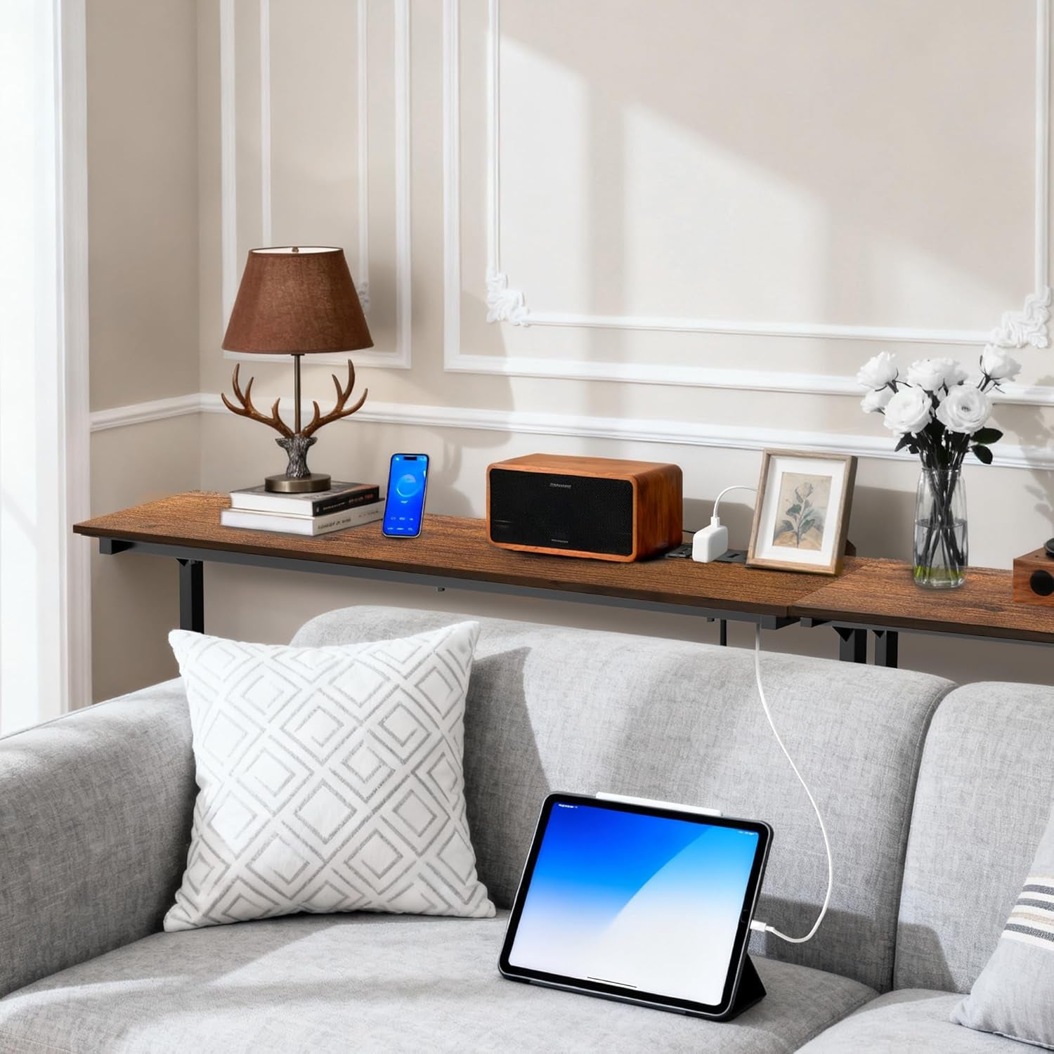 Brown console tables line the back of a gray sofa while a tabletop power panel charges a tablet.