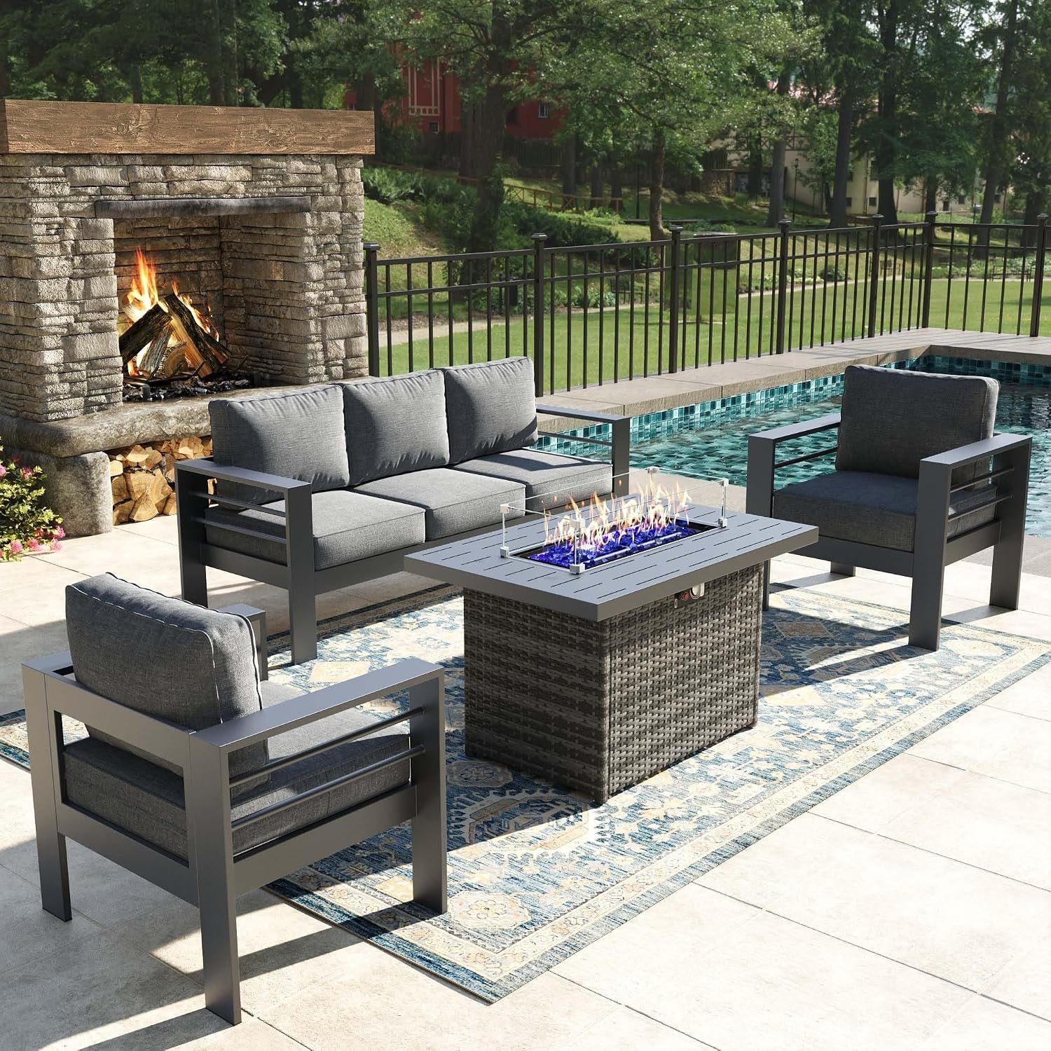 Dark metal-framed seating set around a woven fire table with a gray slatted top beside a pool