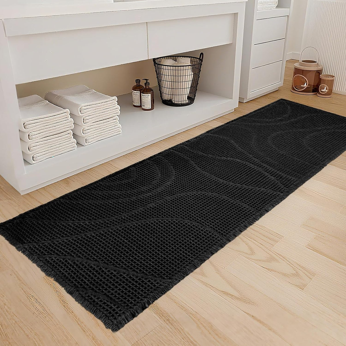 Long black runner with wavy textured pattern placed in front of a white vanity on wood floor.