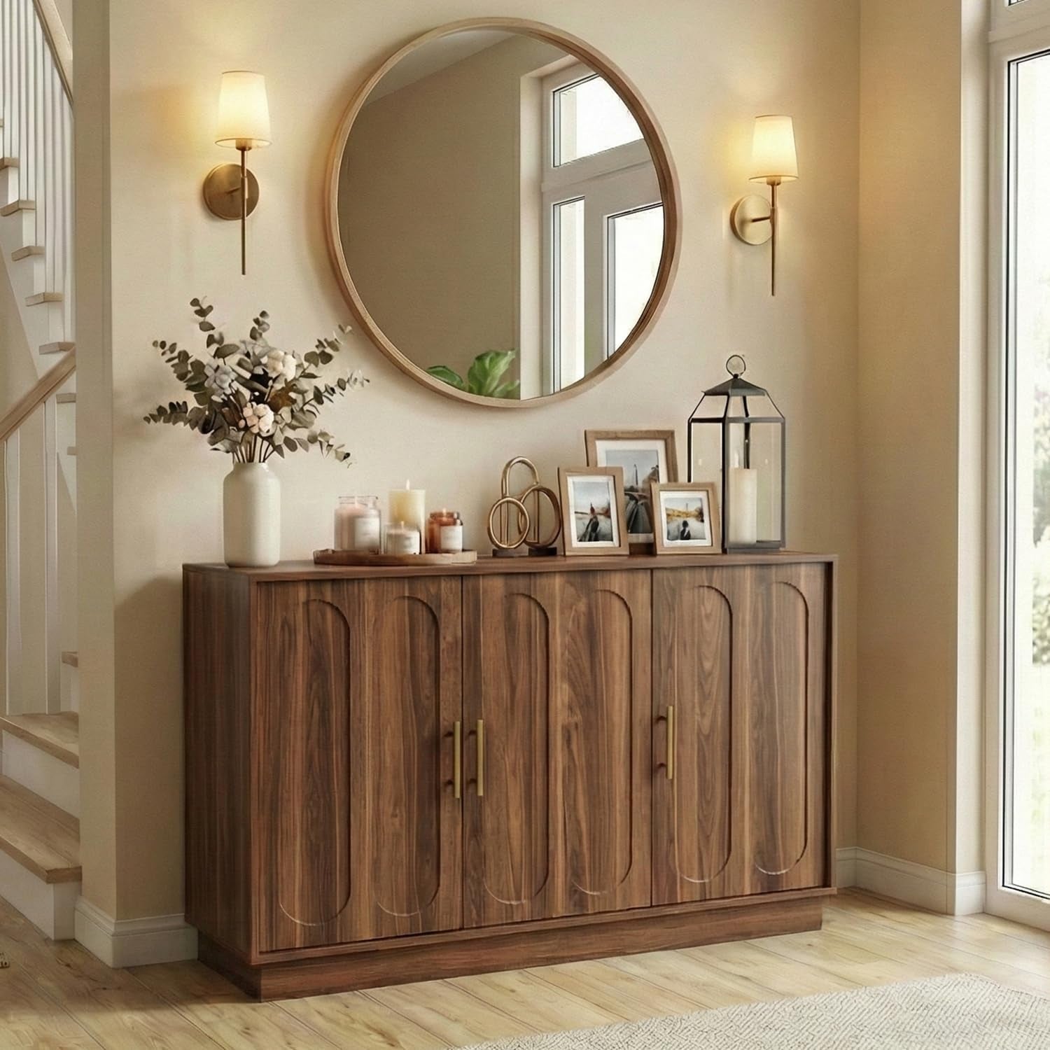 Brown fluted-door storage cabinet styled in an entryway beneath a round mirror with candles and frames on top