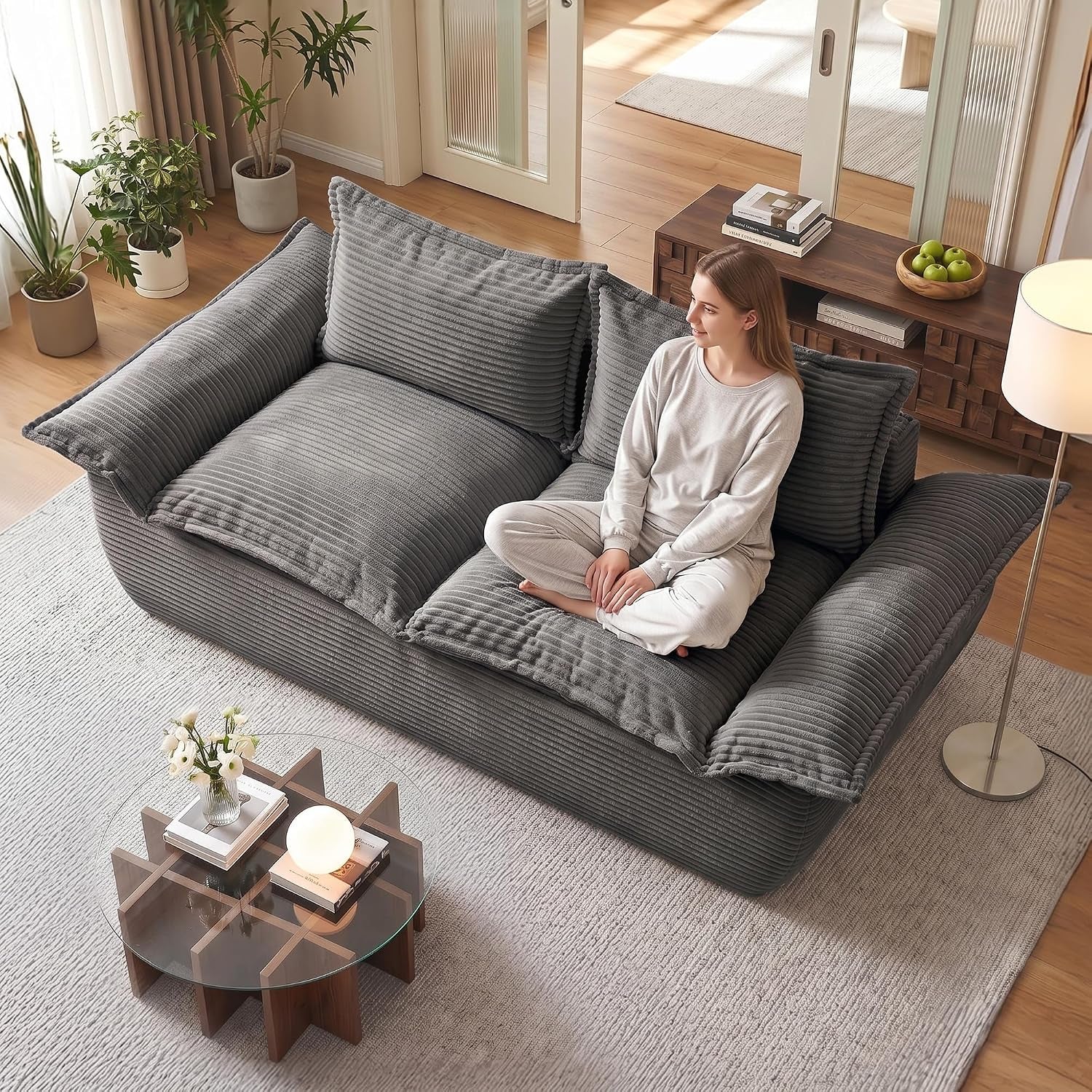 Overhead view of a charcoal-gray corduroy two-seat sofa with a woman sitting cross-legged, rug, coffee table, lamp, and
