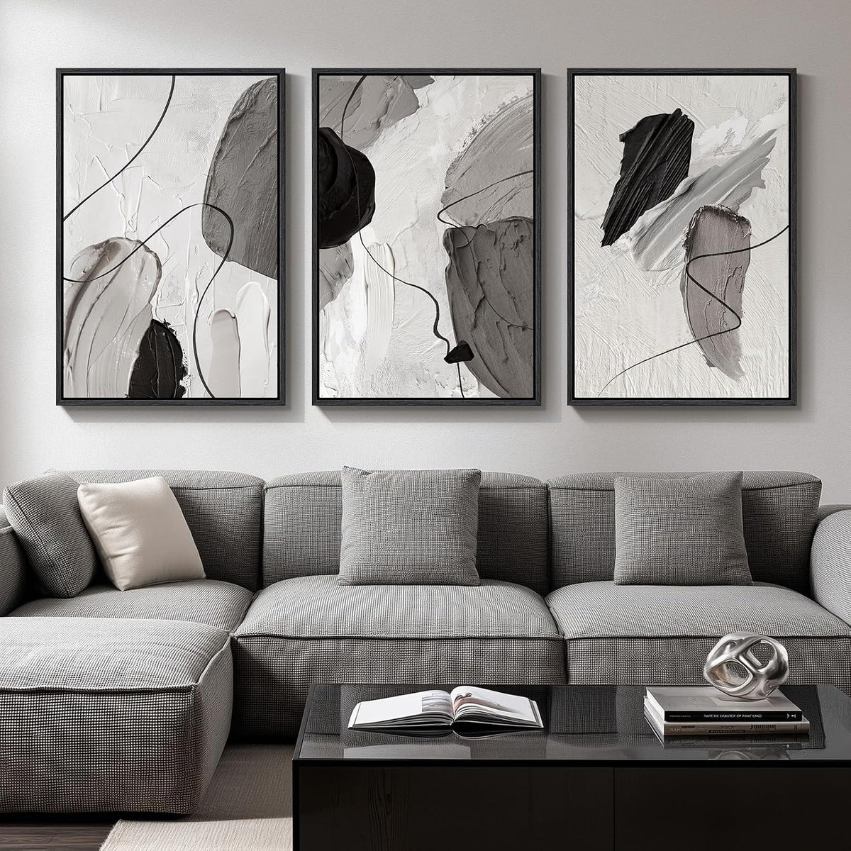Three grayscale abstract framed prints mounted above a light-gray sofa with an open book on the black coffee table.