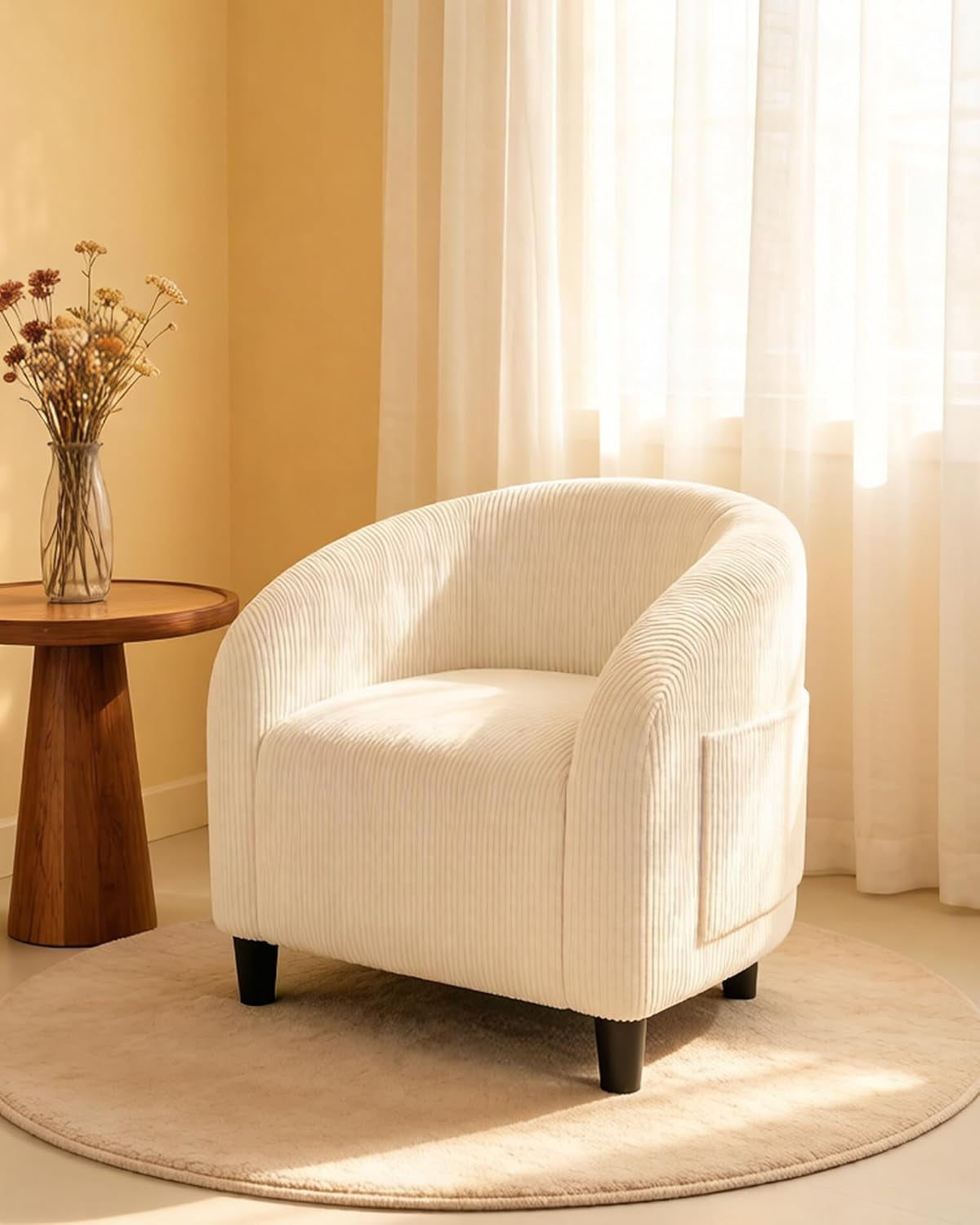 Cream ribbed fabric barrel chair on round rug next to wooden side table and dried flowers