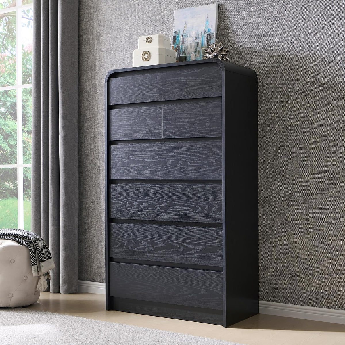 Straight-on view of a tall black chest against a gray textured wall with decorative boxes on top.