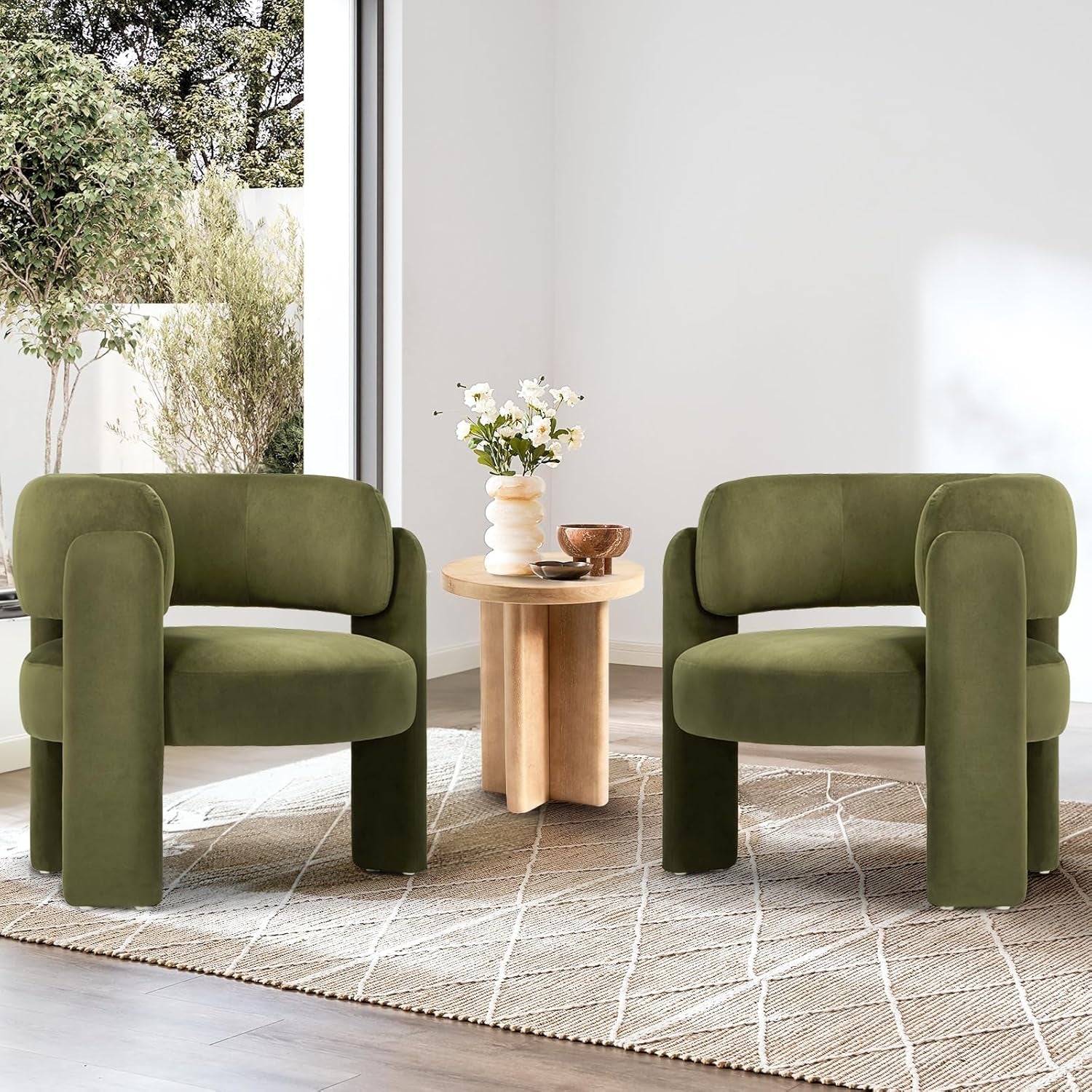 Two olive-green barrel accent chairs flanking a round wooden side table in a bright room