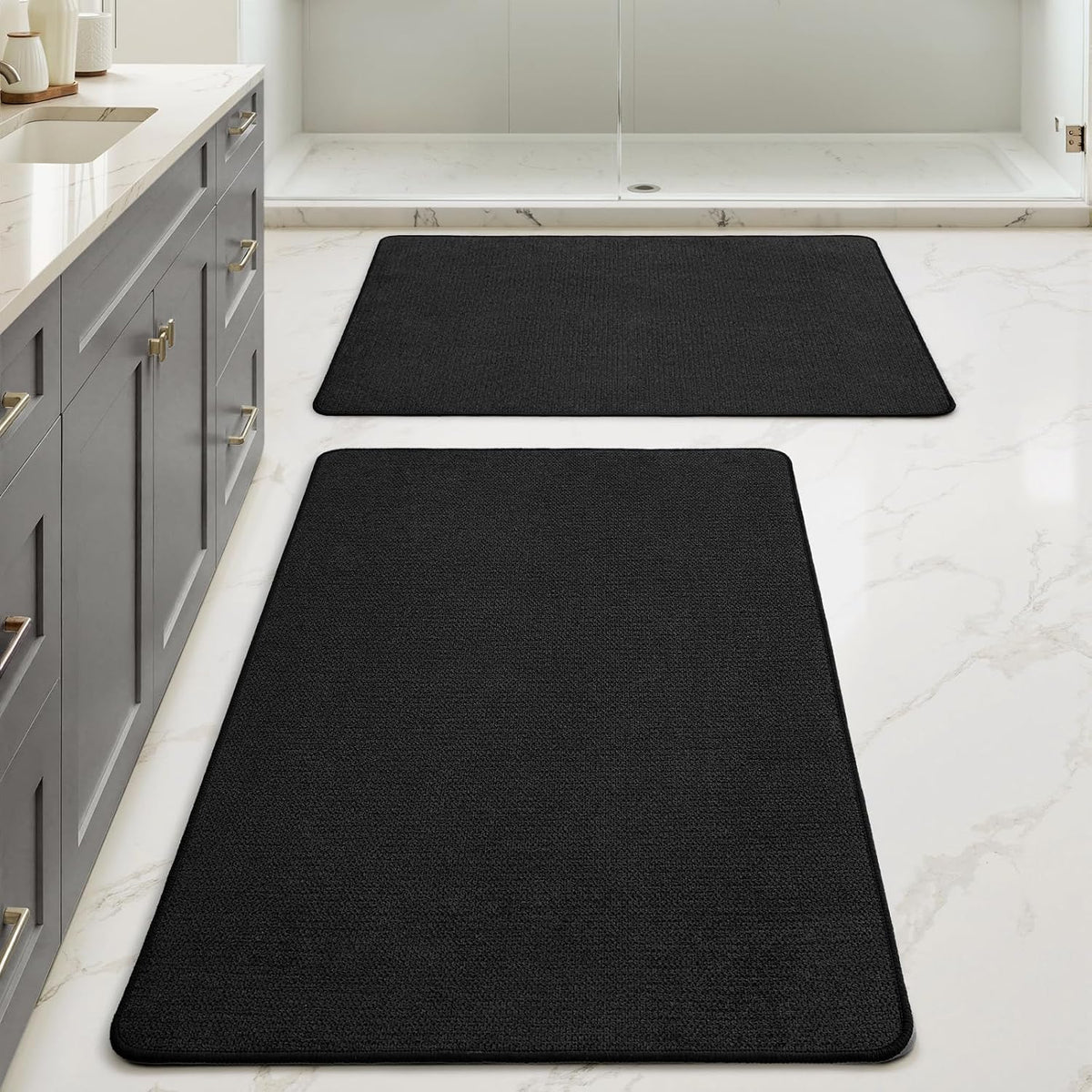 Low-angle perspective of a long black bath runner in foreground with a smaller matching mat near the shower in the