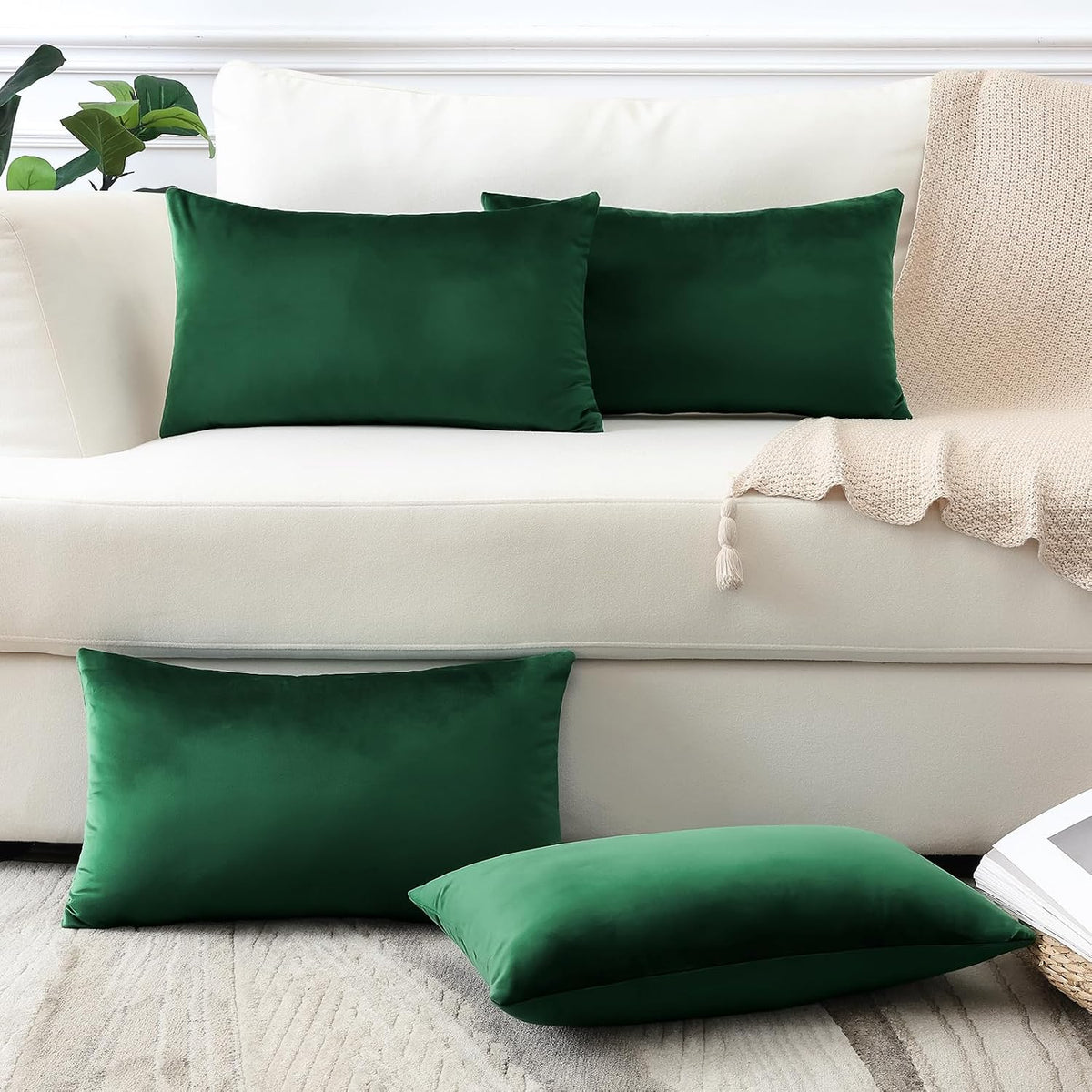 Two emerald green rectangular velvet pillows on a cream sofa with a knit throw and matching floor pillows.