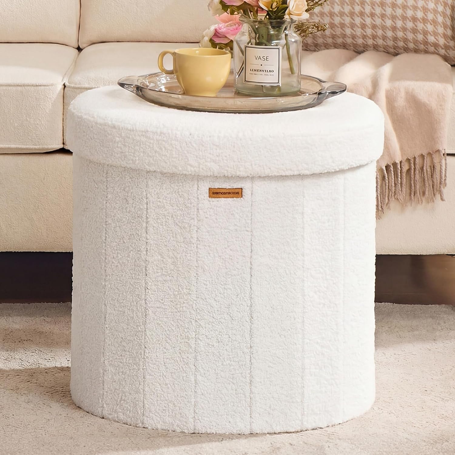 White round storage ottoman beside a sofa with a tray, yellow cup, and vase on top.