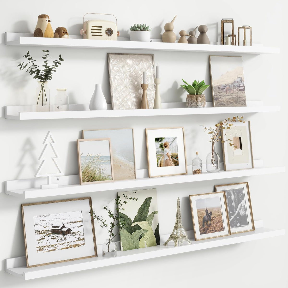 Three white floating picture ledges mounted on a white wall with framed art and decor.