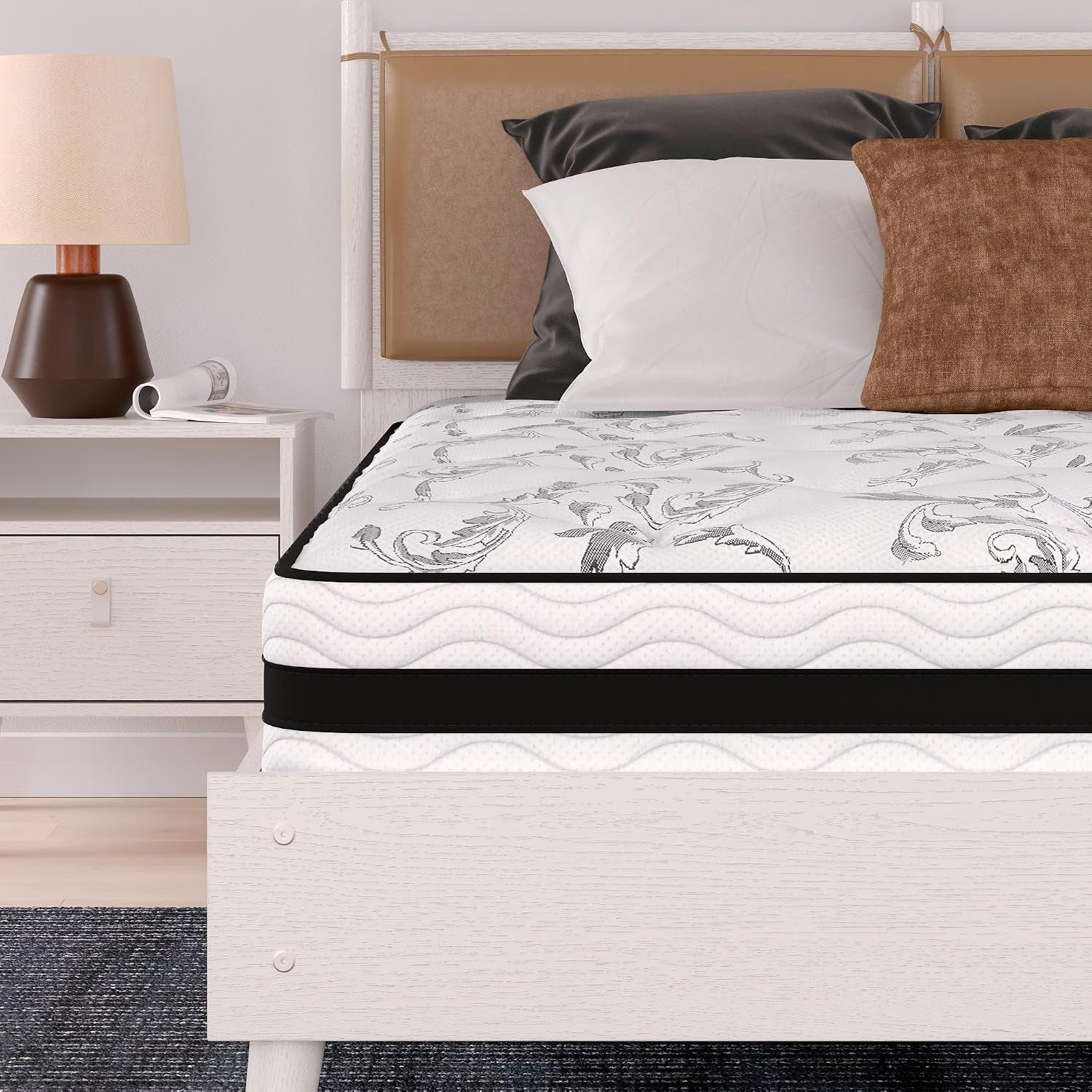Close-up of mattress corner showing white quilted top, black horizontal band and layered profile next to a nightstand and