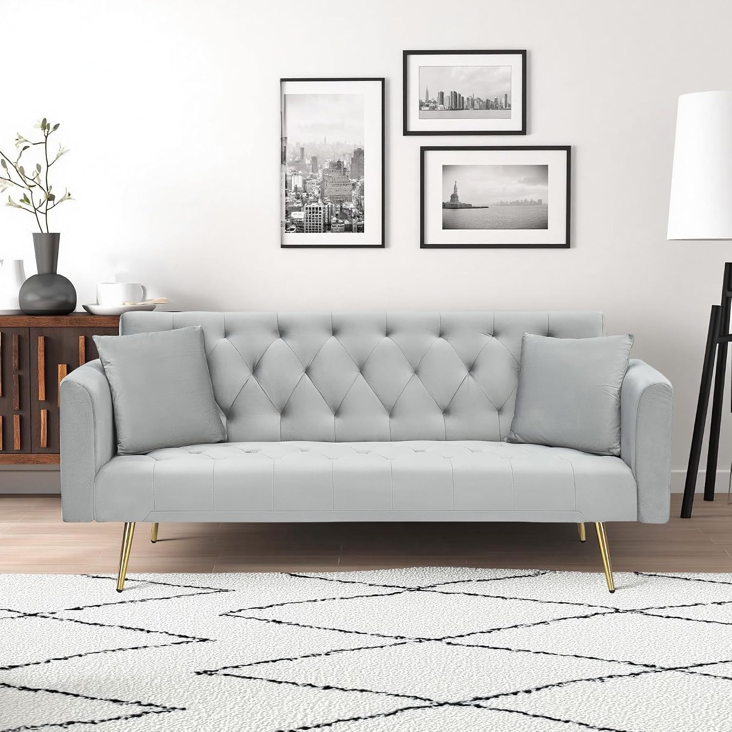 Front view of a light gray velvet tufted sofa with gold legs and two matching pillows on a patterned rug.