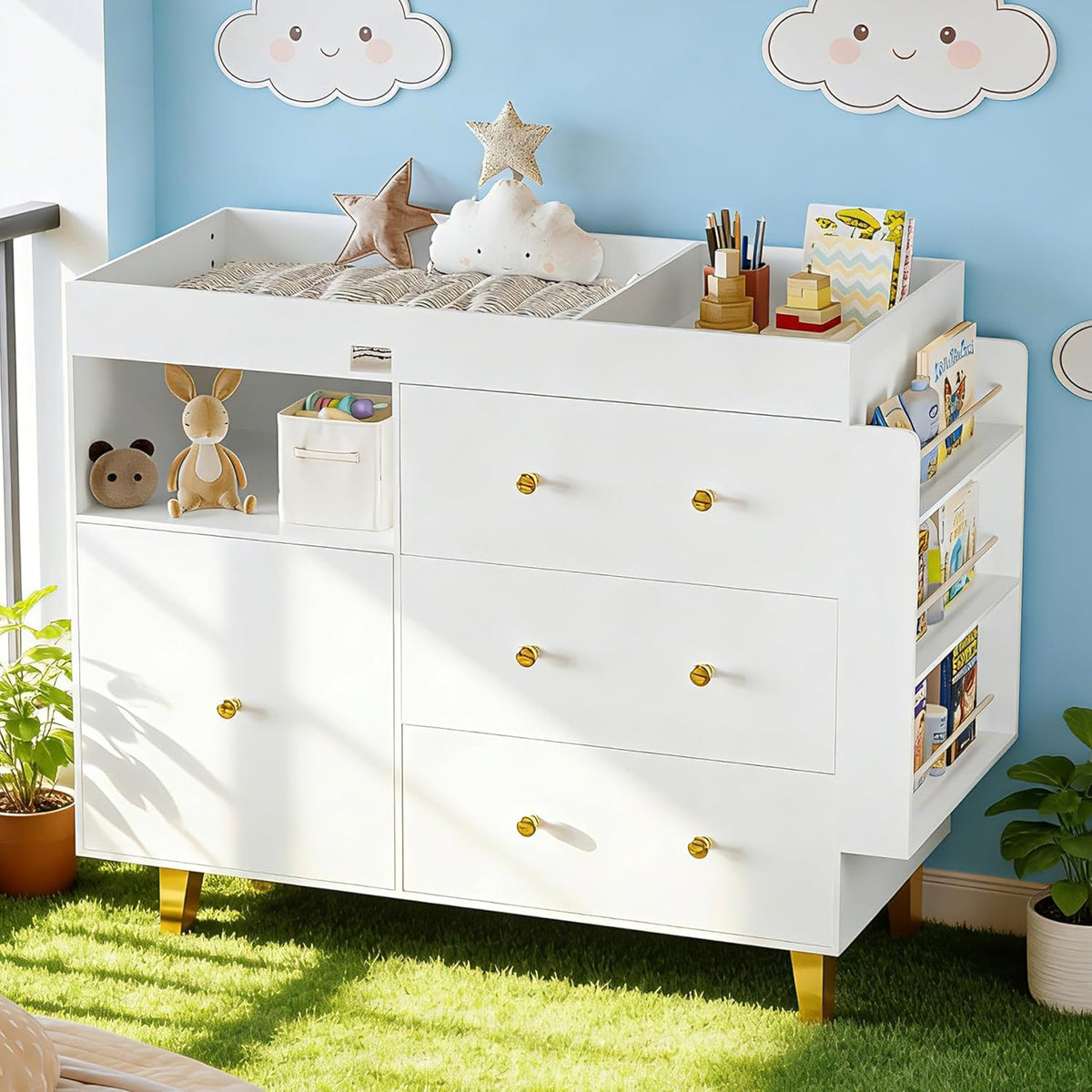 White changing dresser with raised changing top, gold knobs and legs, side book shelves and toys on open cubbies