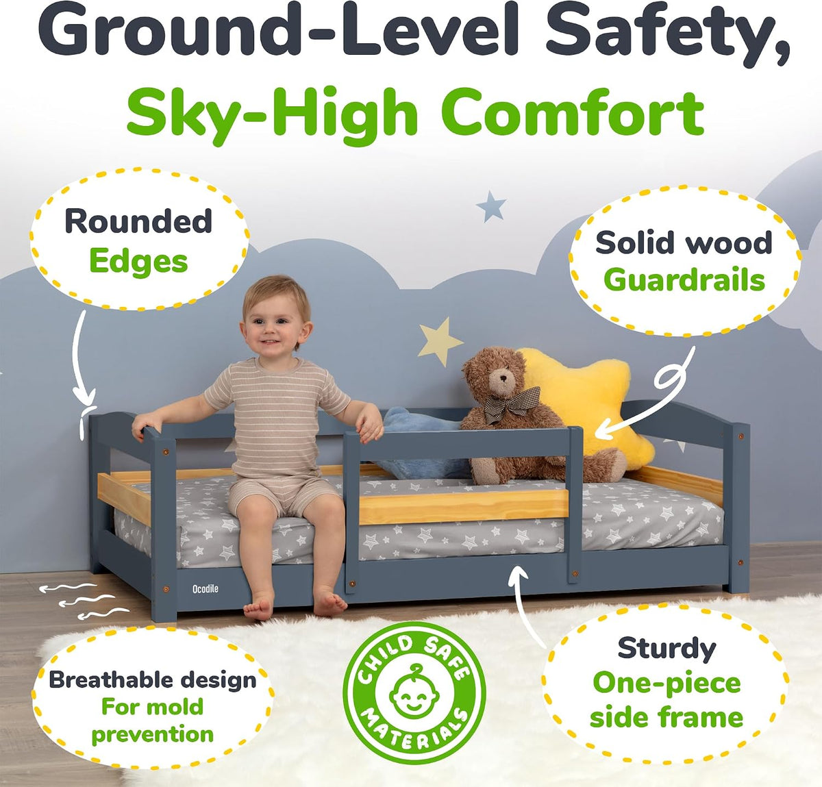 Main room shot: toddler sitting on low gray bed with wooden inner rail, teddy and star pillow, graphic callouts and green