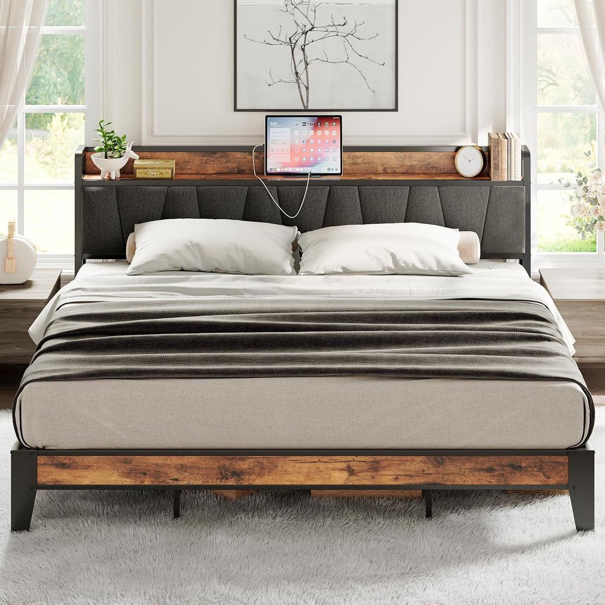 Dressed bed front view showing upholstered headboard shelf holding a tablet with a visible charging cable and bedside decor