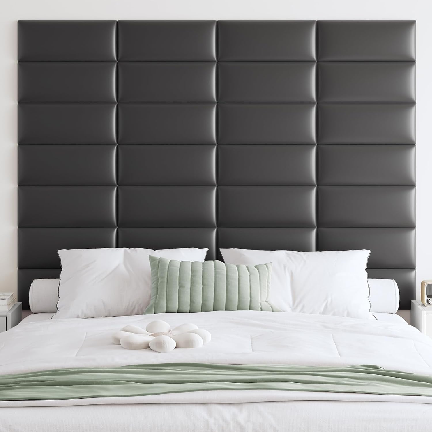 Dark charcoal padded headboard panels in a grid pattern behind a bed dressed in white linens and a pale green throw.