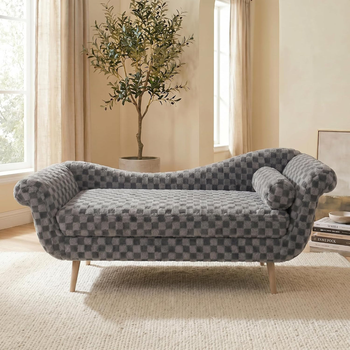 Front view of a gray checkered chaise lounge in a sunlit room with a potted olive tree behind it