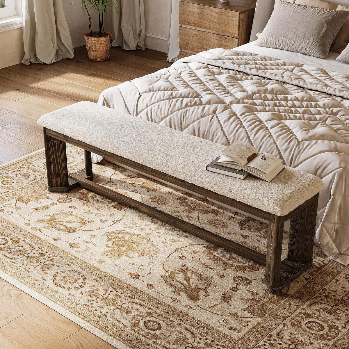 Angled bedroom view of a long fur-top bench on a patterned rug with an open book resting on the seat.