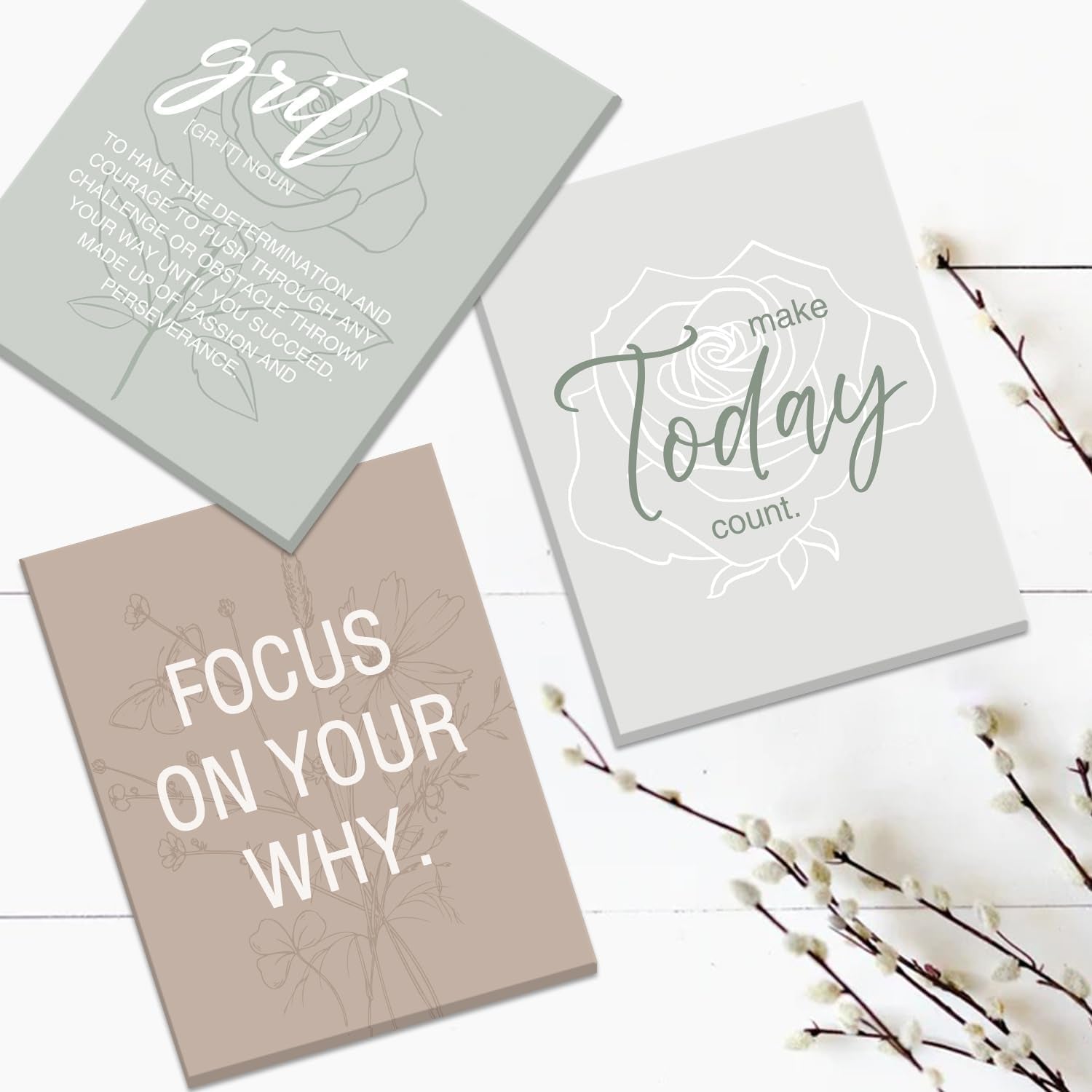 Close-up of three loose canvas prints on a white wood surface showing 'Focus On Your Why' and floral line art