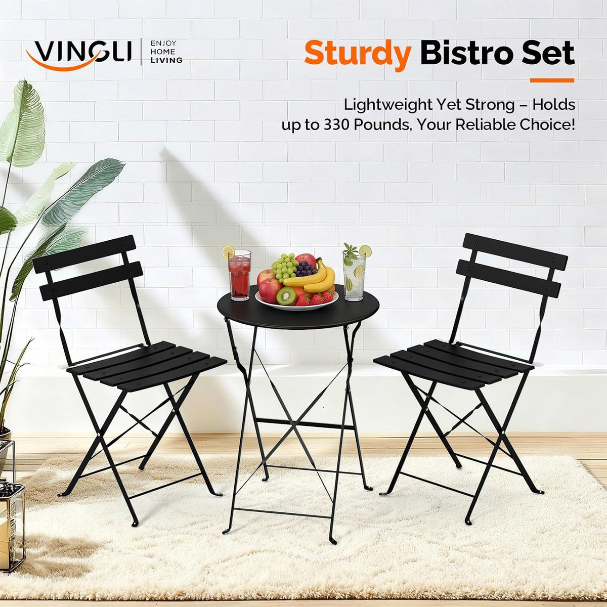 Black bistro table and two chairs staged indoors with fruit and drinks on the table, front view