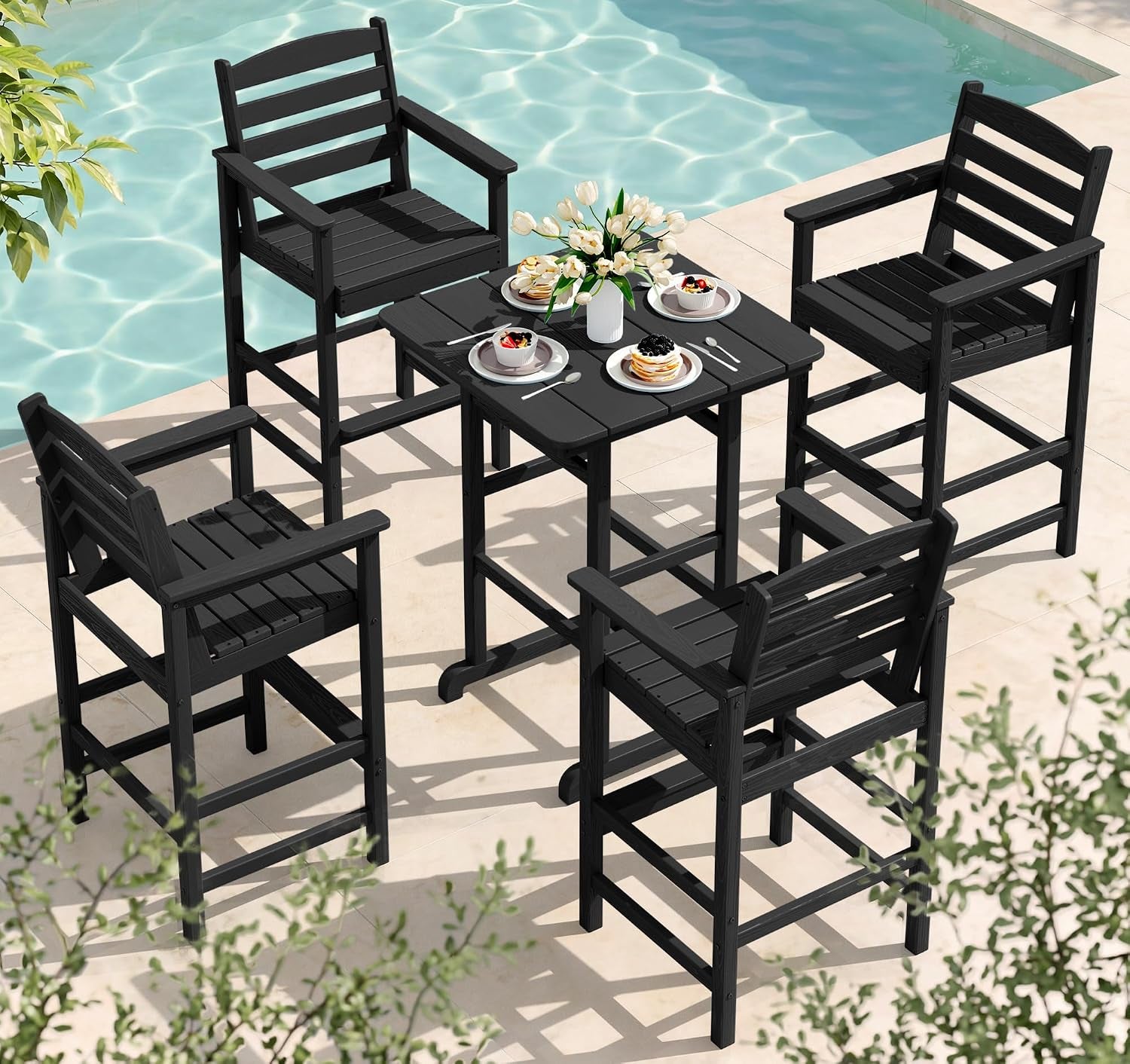 Black square bar table surrounded by four black bar-height armchairs near a pool with place settings