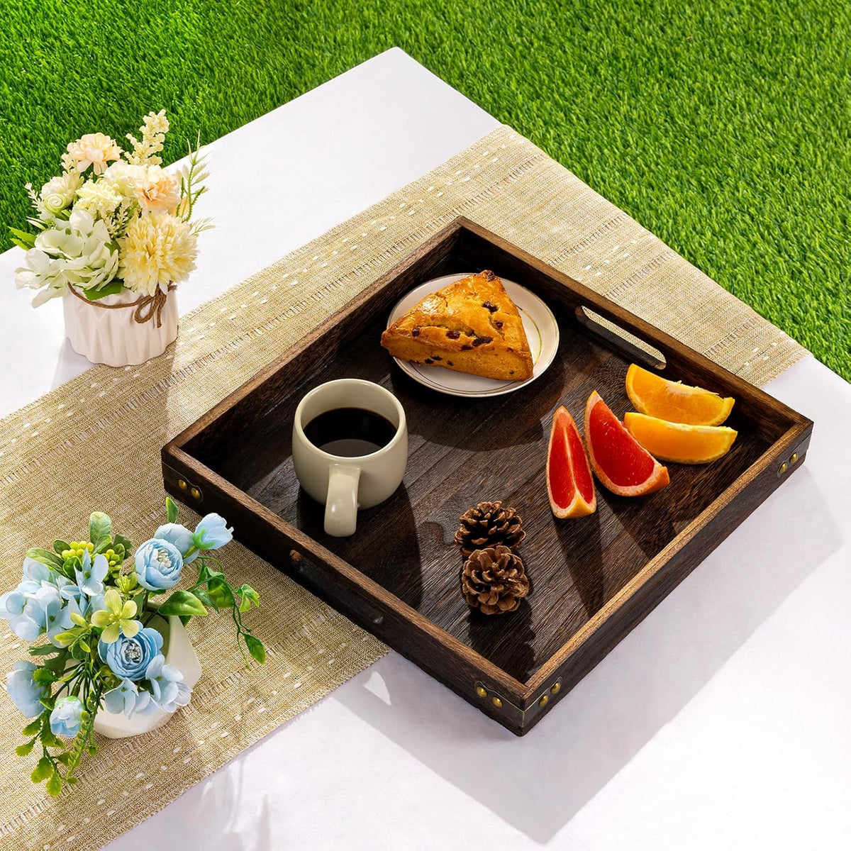 Close-up tabletop scene of a dark wood square tray displaying a coffee mug, scone and sliced citrus on a placemat
