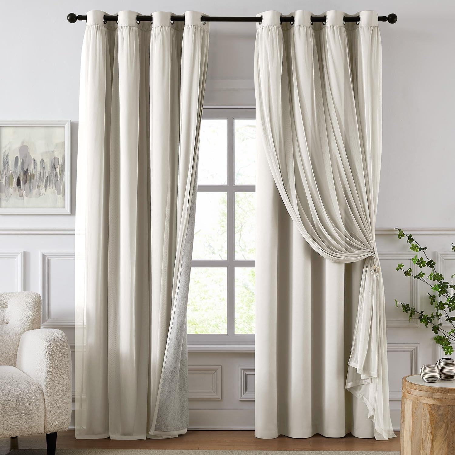Window with two layered ivory curtains, sheer drape tied on right, upholstered chair left