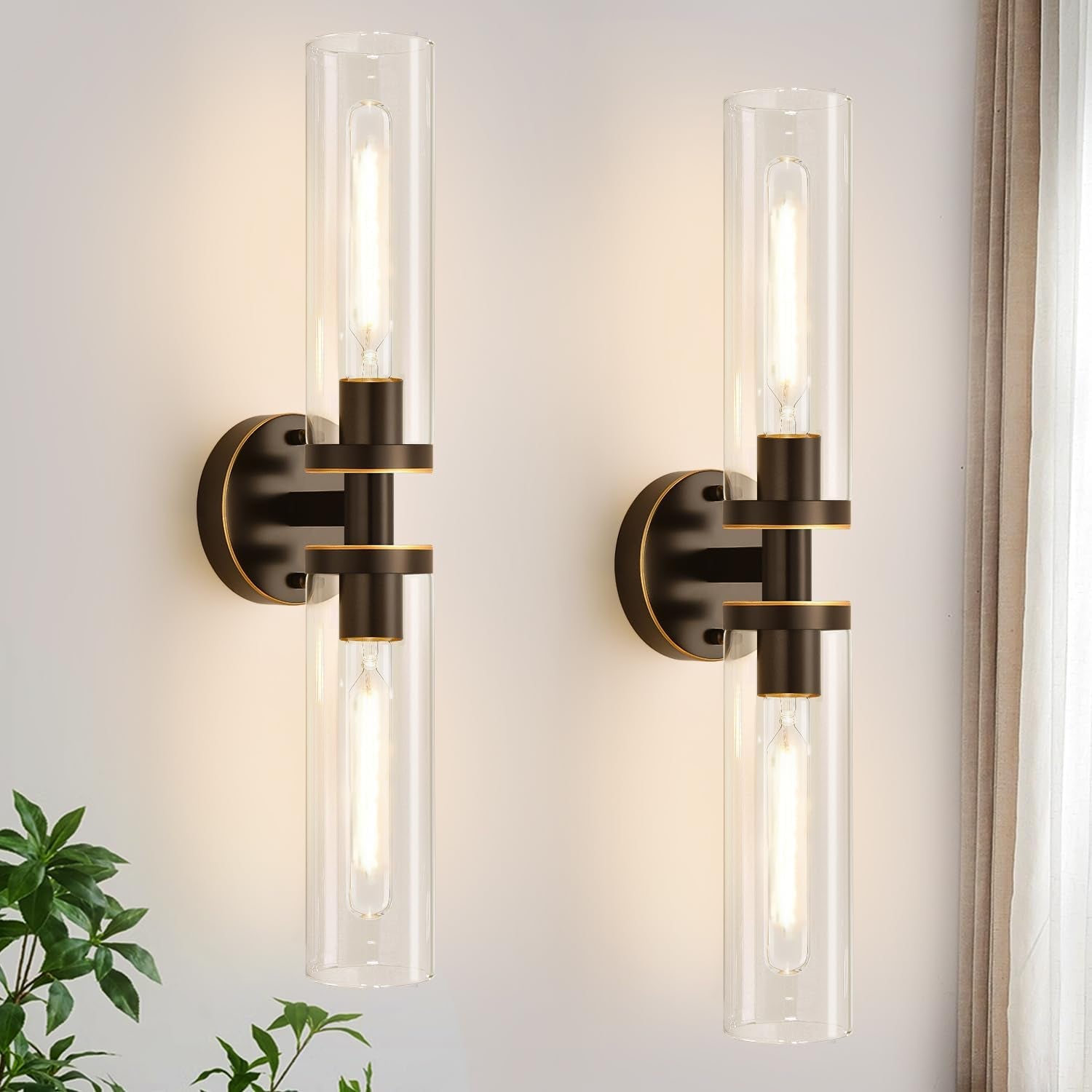 Close-up of two mounted sconces showing black metal accents and clear cylindrical glass shades lit warmly.