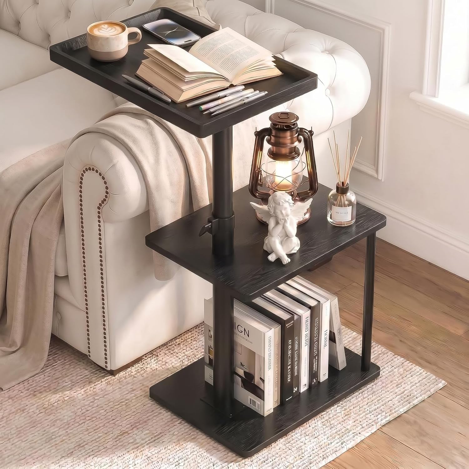 Black three-tier C-shaped side table styled with a cup, book, lantern and stacked books below