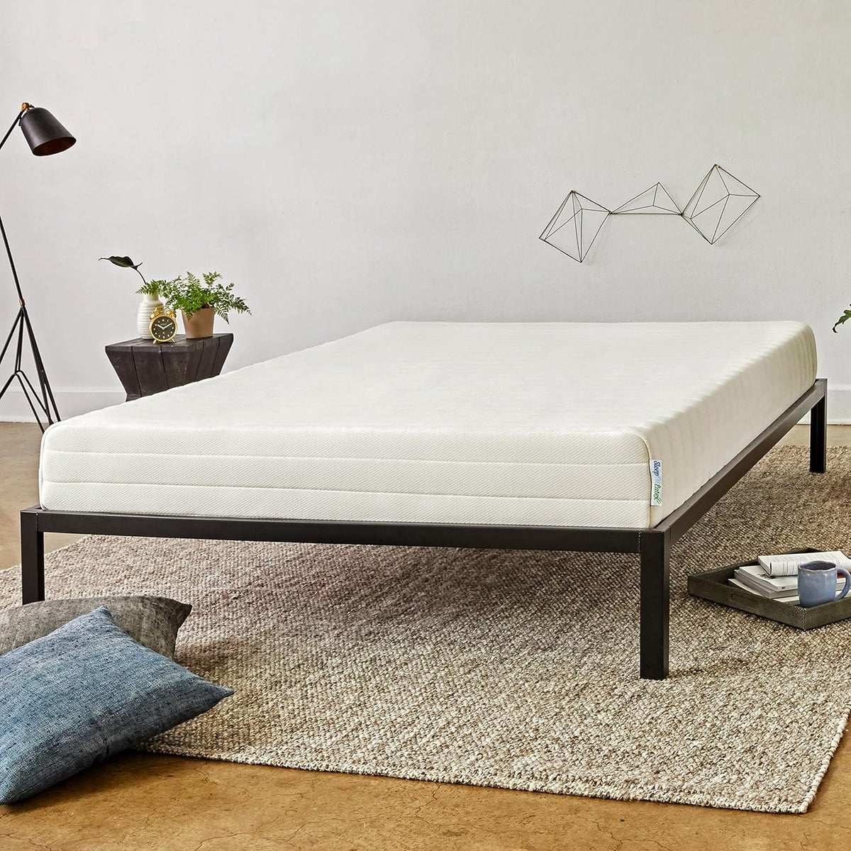 Full view of a cream organic latex mattress on a low black metal platform bed in a bright bedroom.