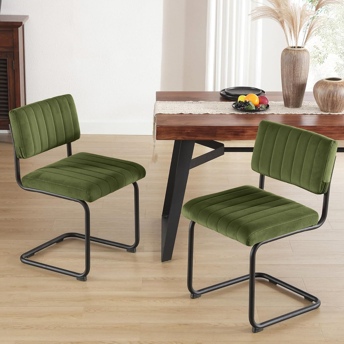 Two green velvet dining chairs beside a wooden dining table in a room setting, front view of tufted backs and seats