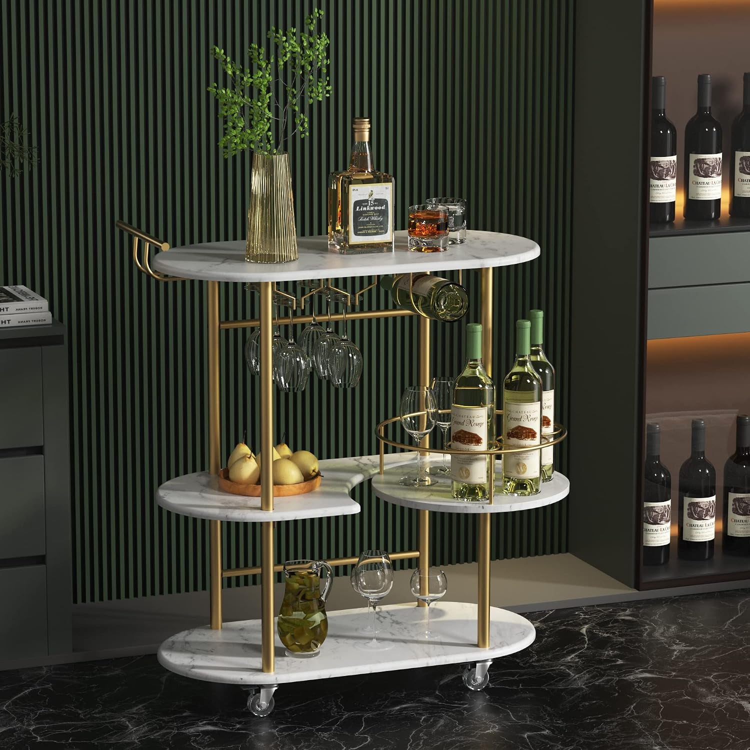 Three-tier gold and white marble bar cart in a dark room with bottles, glasses and a vase on top.