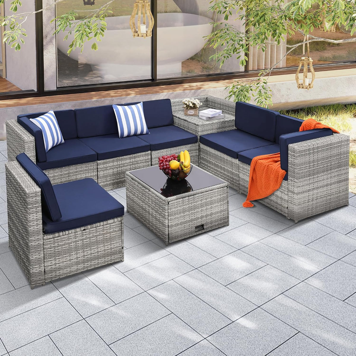 Light gray wicker modular seating arranged outdoors with navy seat cushions, glass-top coffee table and orange throw.
