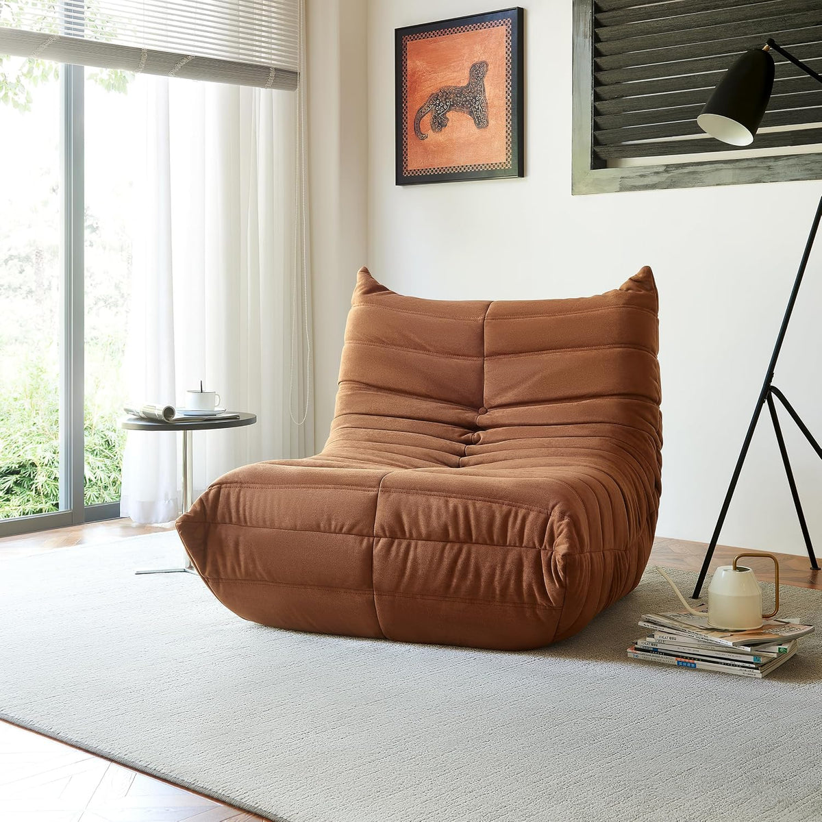 Rust-colored single bean bag chair in a sunlit room with floor lamp and stacked magazines beside it.