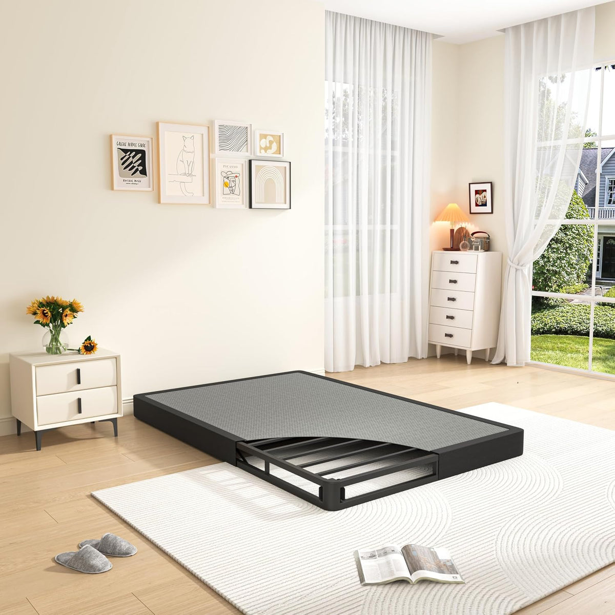 Angled view of a low black metal mattress foundation with pulled-out slatted support in a sunny bedroom