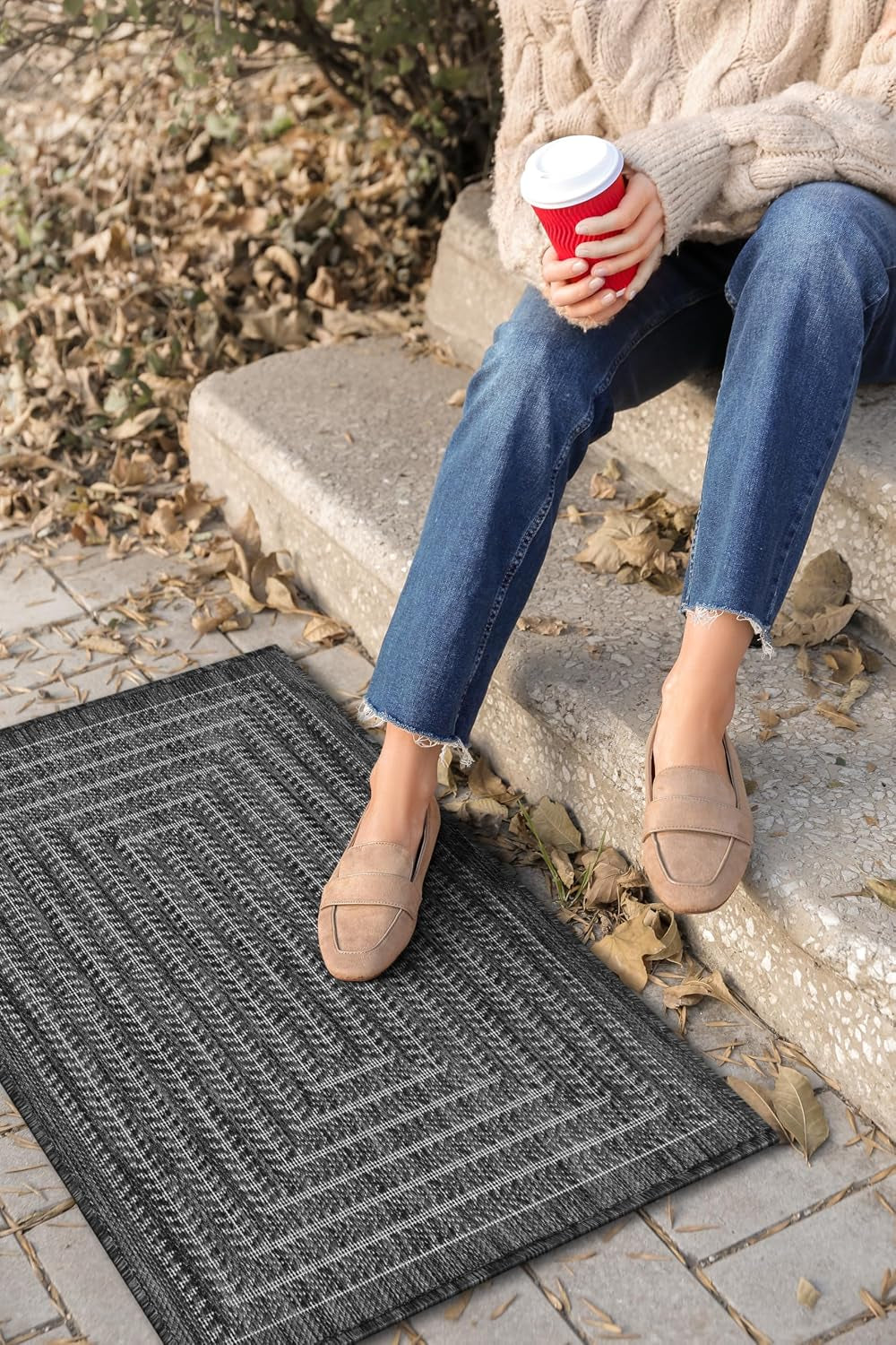 Small dark-gray outdoor rug beside concrete steps while a person sits holding a coffee cup