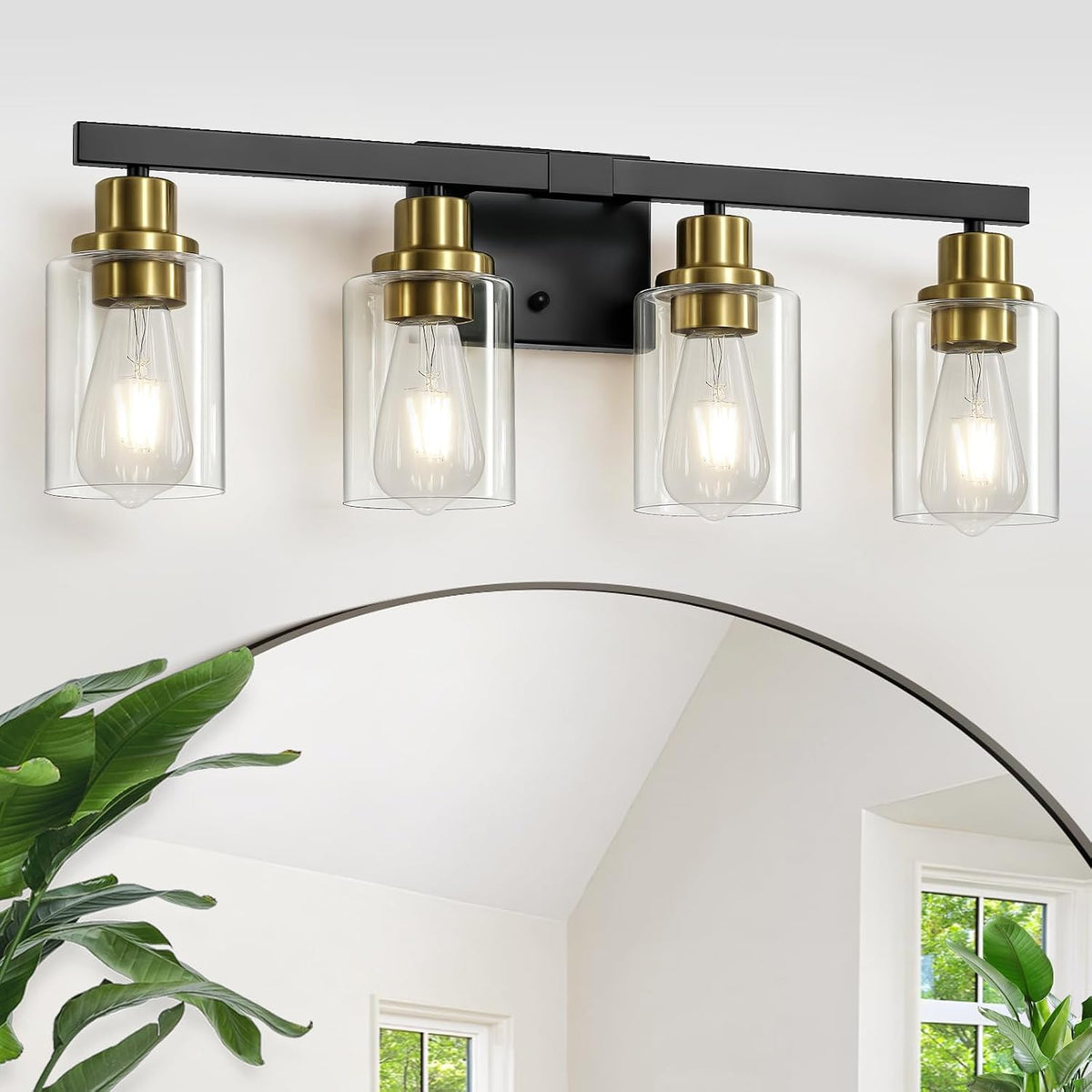 Close angled view of the four-bulb fixture with clear cylindrical shades above a rounded mirror and leafy plants.