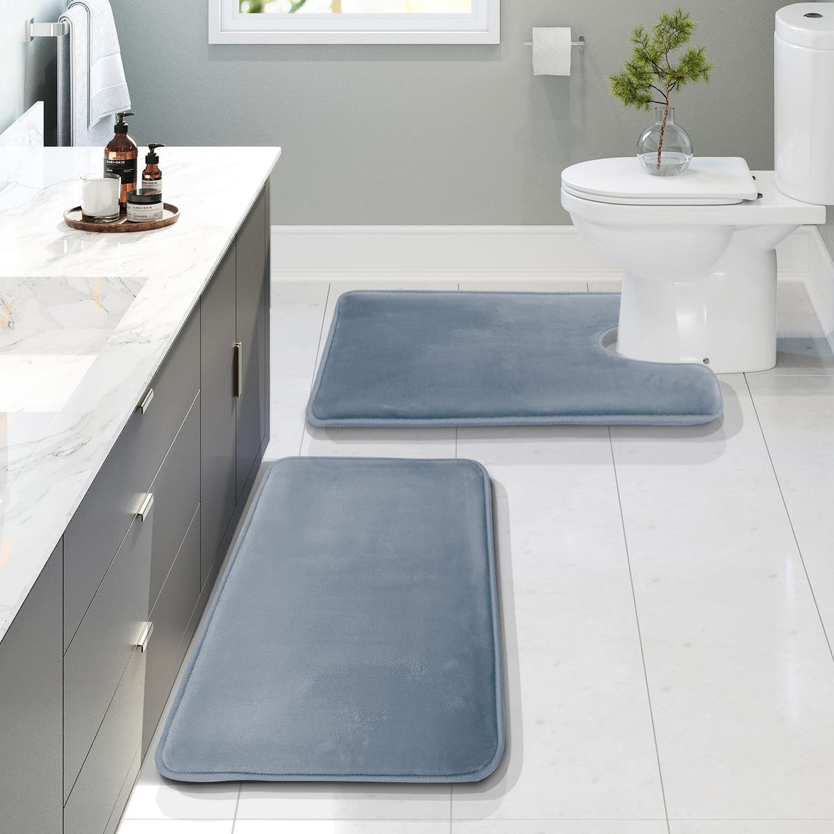 Bathroom scene with three blue memory-foam bath rugs—two rectangular runners and a U-shaped rug at the toilet.