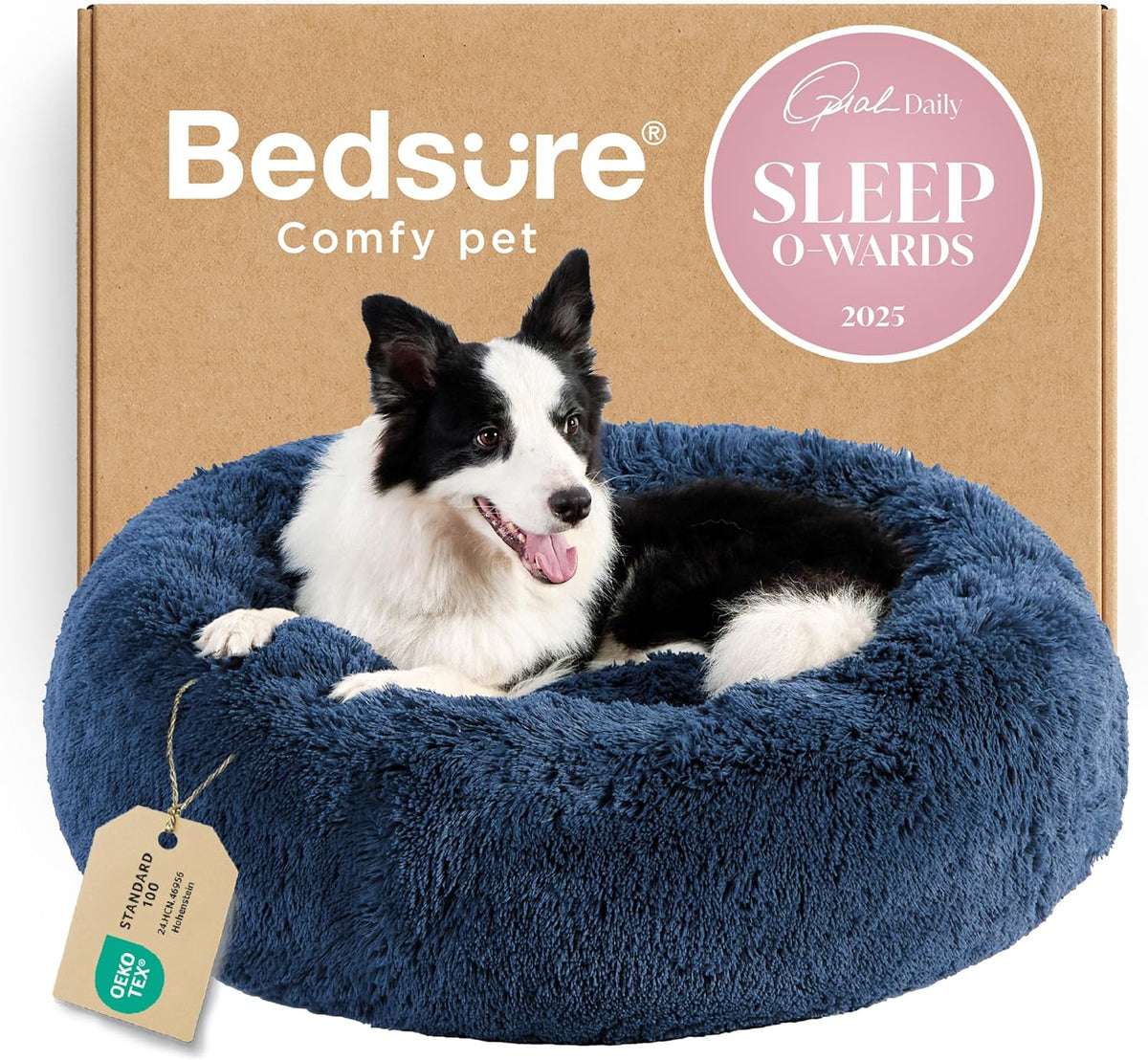 Black-and-white dog resting in a deep blue donut bed in front of a cardboard box, tag visible on rim.