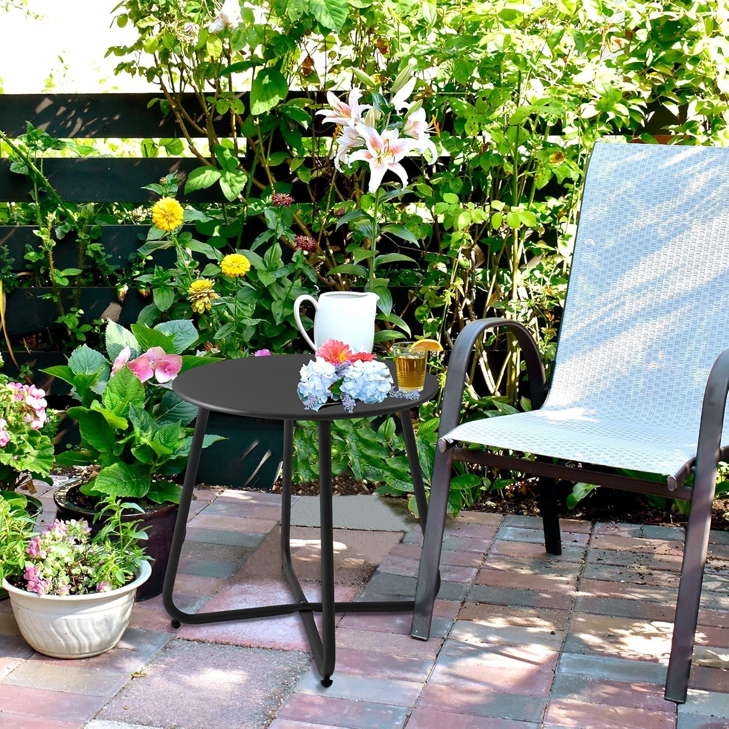 Black round side table placed on a brick patio beside a lounge chair with plants