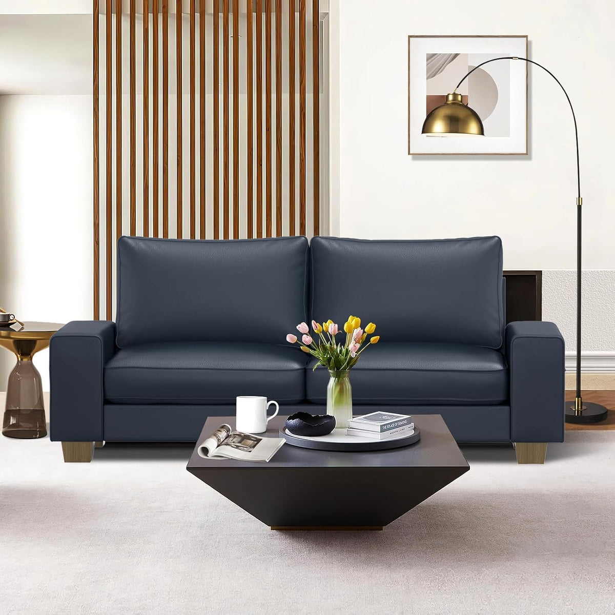 Front view of a navy-blue faux-leather loveseat with a tulip vase on the coffee table and floor lamp beside it
