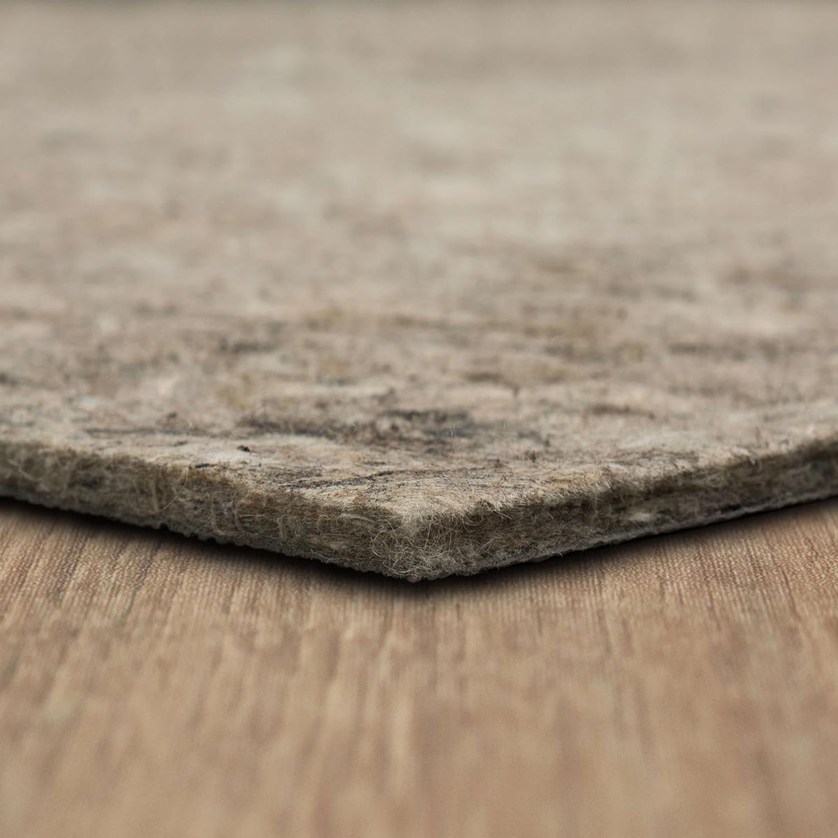 Macro profile of the pad edge resting on a wood surface, highlighting loose felt fibers and layered texture.