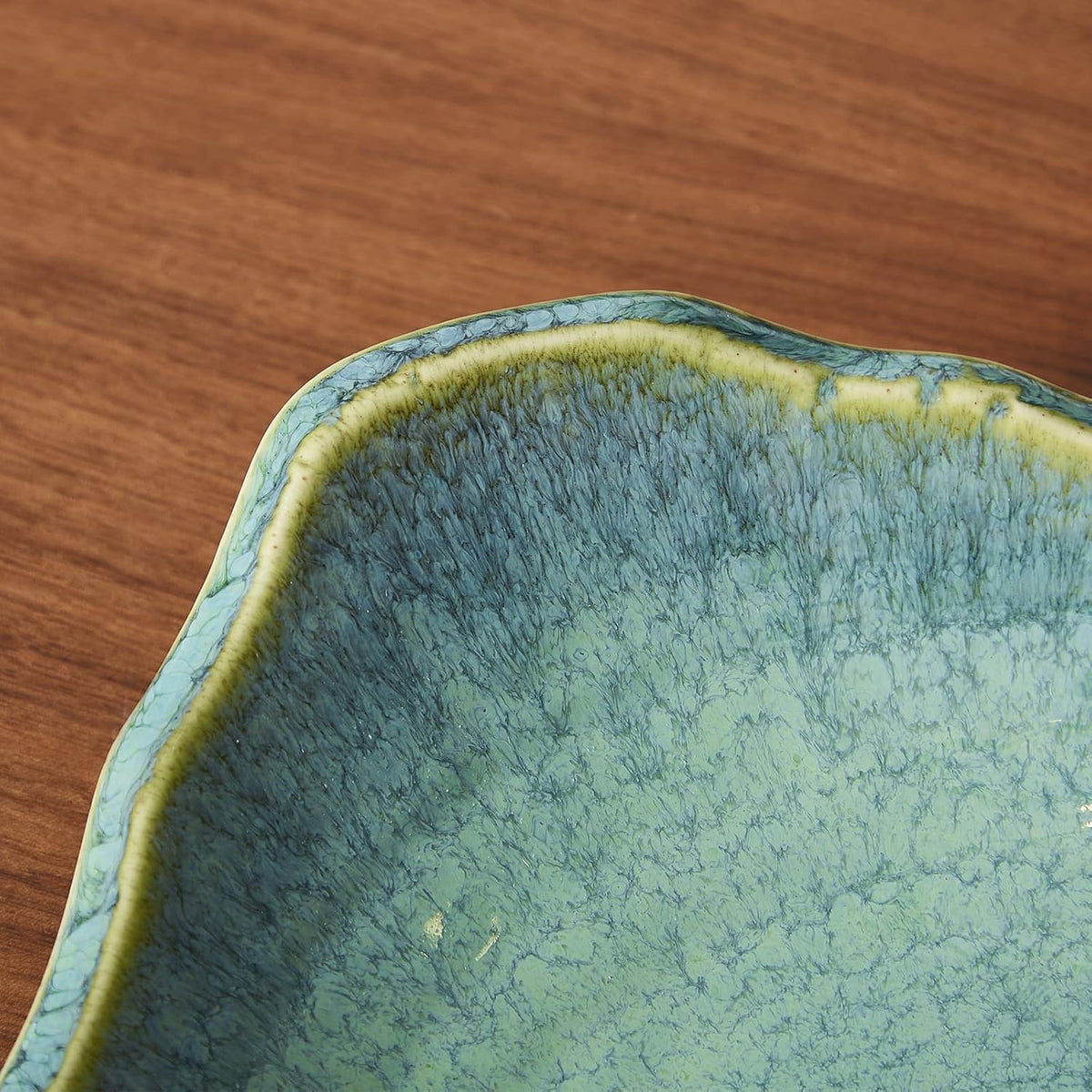Close-up detail of green crackle glaze and yellow-tinted irregular edge of the ceramic bowl