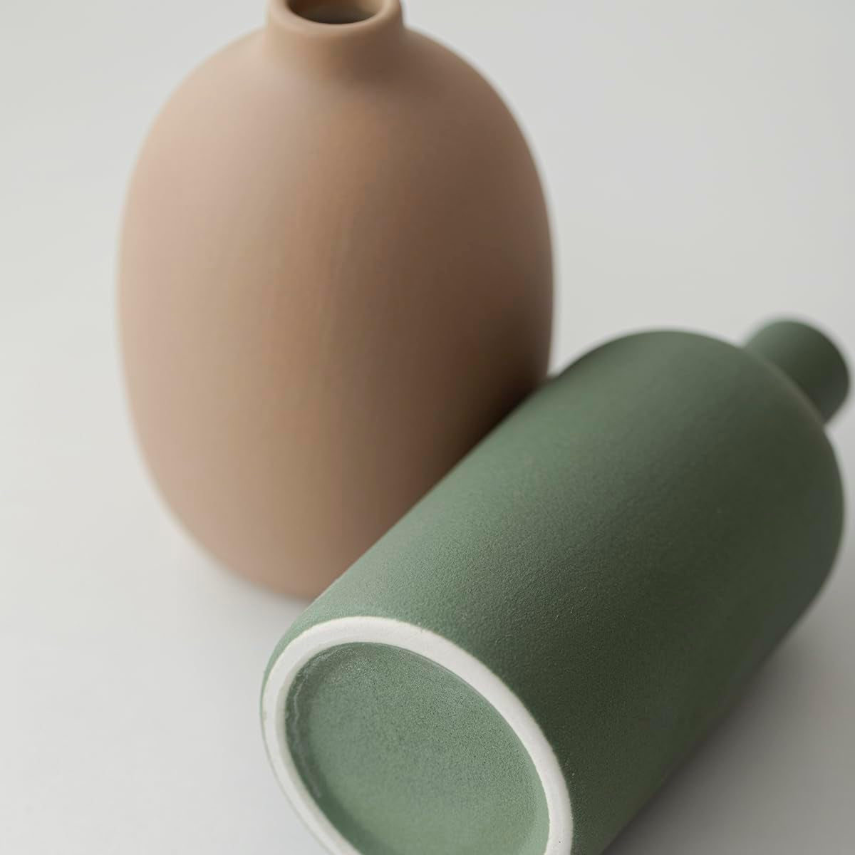 Close-up angled view showing the unglazed white base ring and matte green surface texture of one vase
